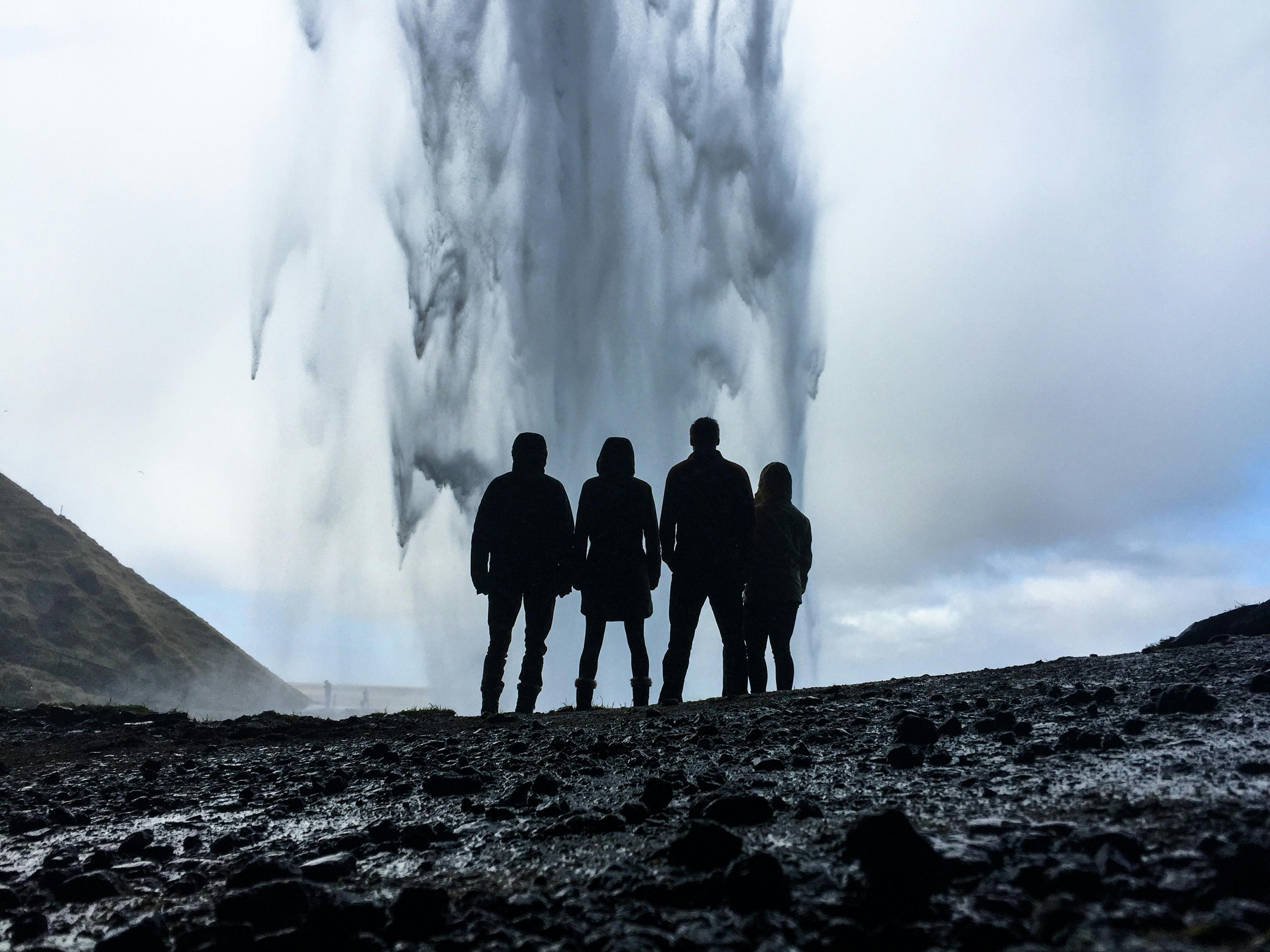 Silhouetted figures stand in awe before the powerful Seljalandsfoss waterfall in Iceland, framed by mist and overcast skies.