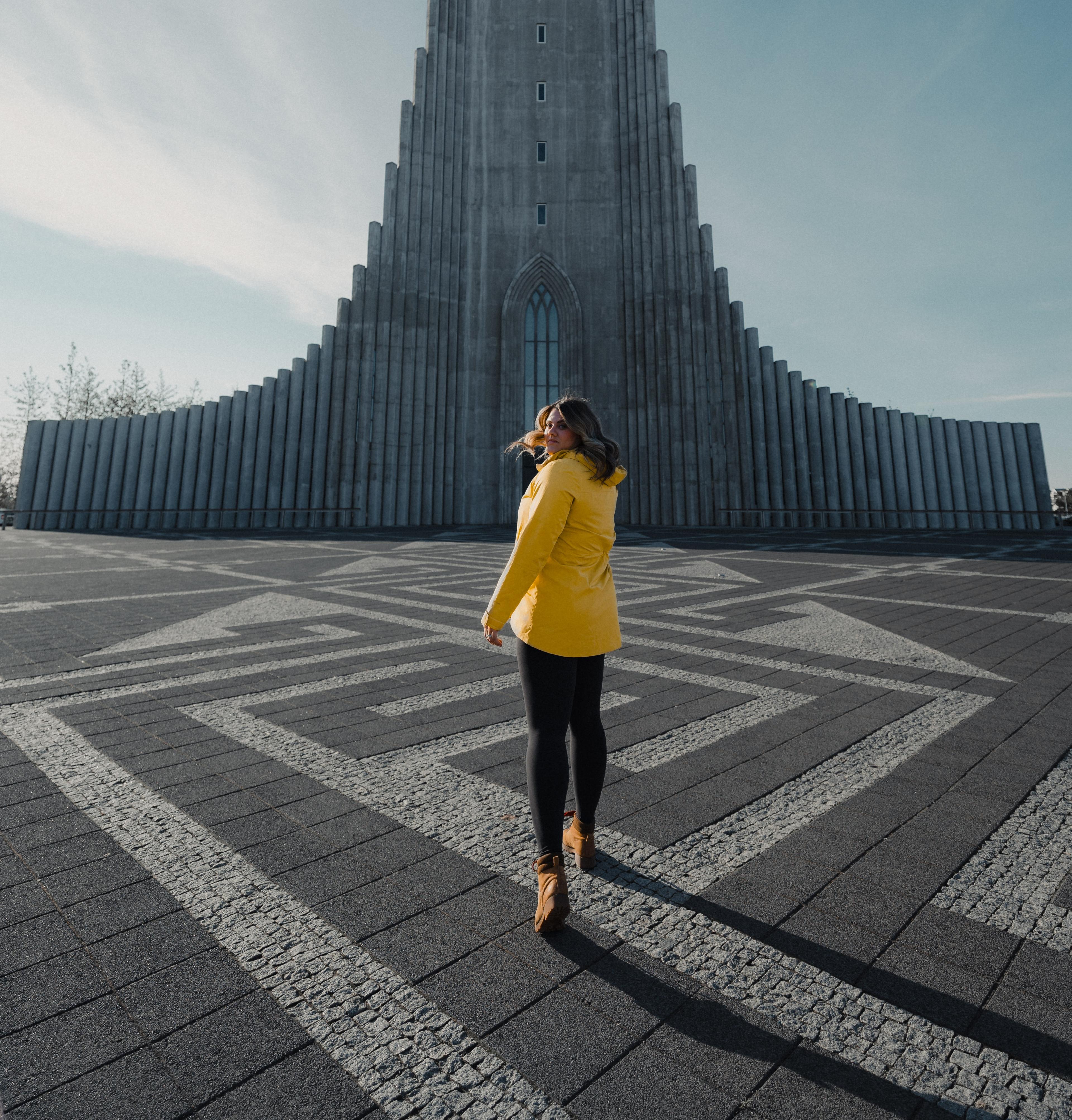 A woman in a light yellow jacket strolling towards the Hallgrimskirkja church, bathed in sunshine.