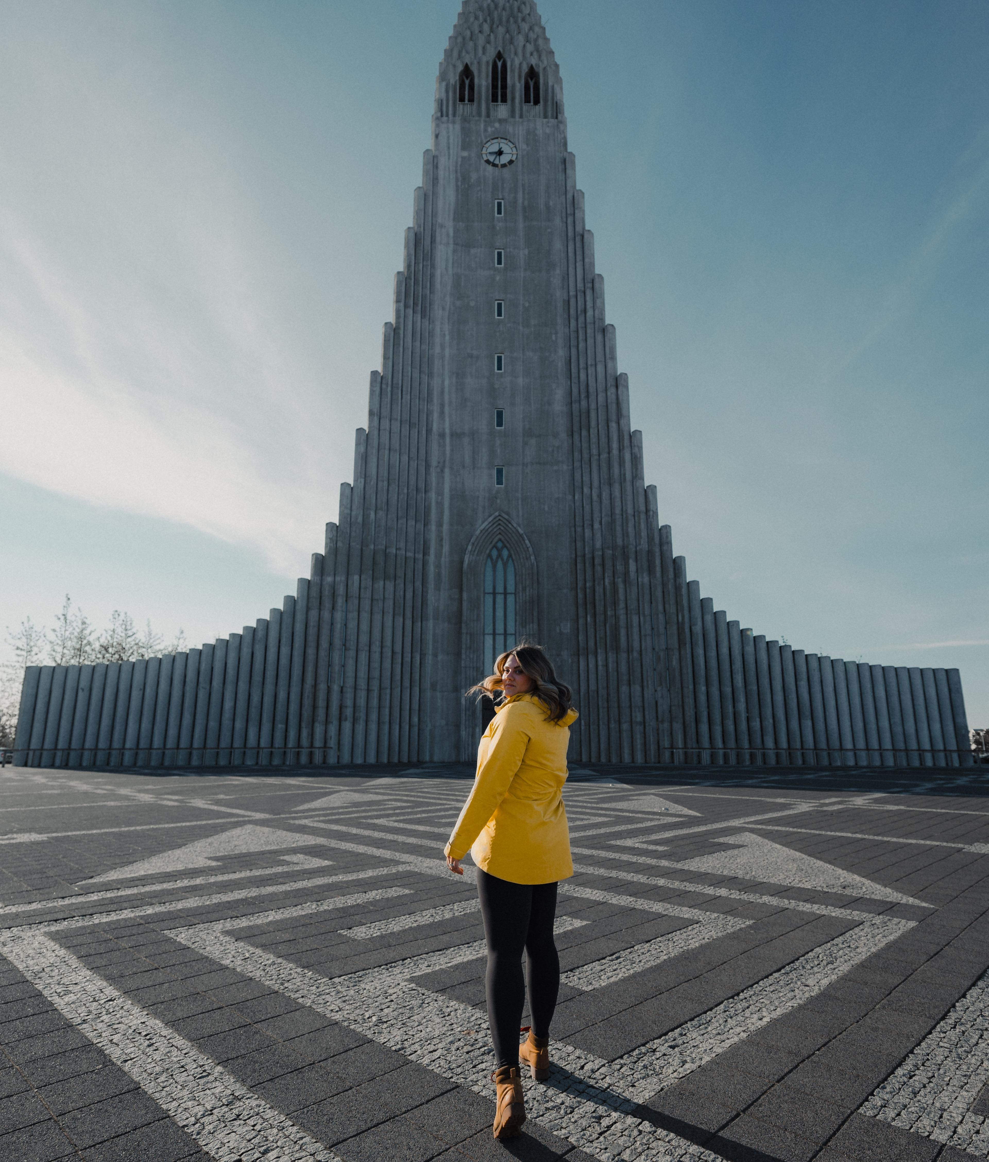 A woman in a light yellow jacket strolling towards the Hallgrimskirkja church, bathed in sunshine