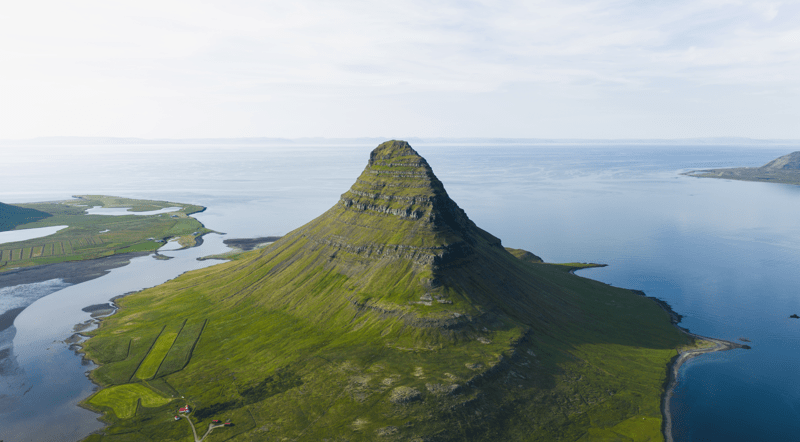 Aerial view of Kirkjufell, a conical green mountain, surrounded by water.