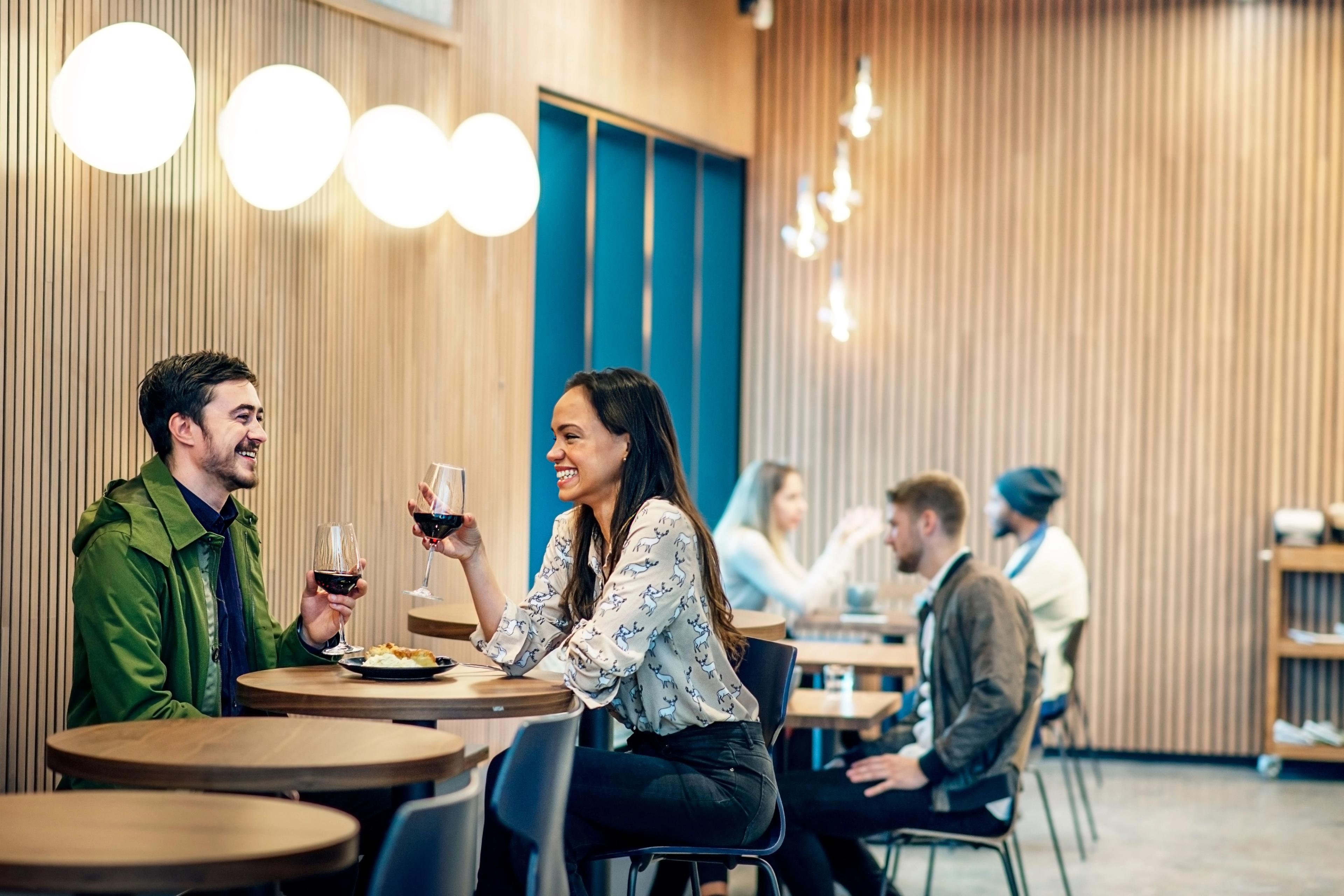 A smiling couple toasts with red wine in a modern restaurant.