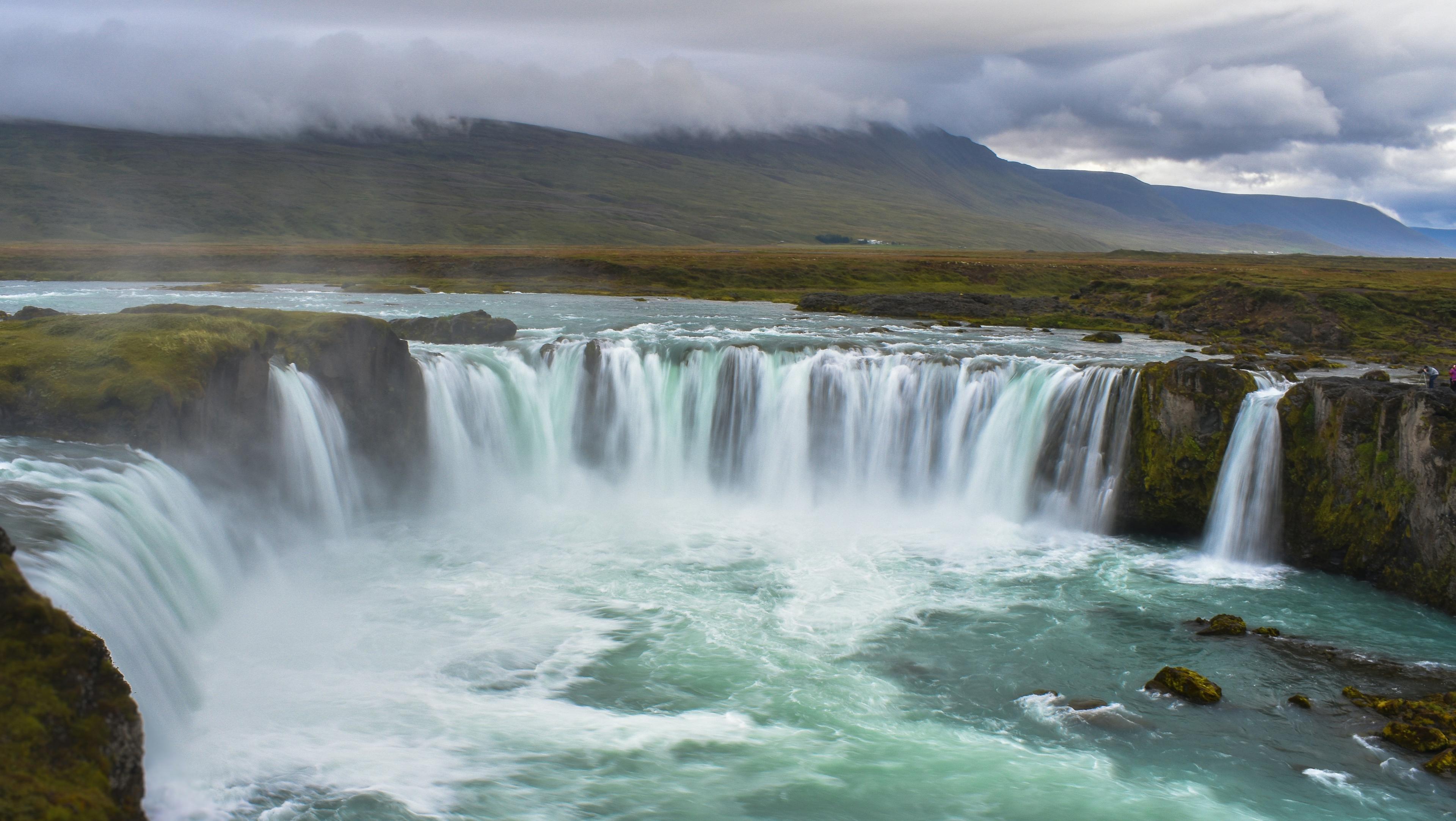 Scenic view of Goðafoss waterfall in Iceland, with powerful cascading water surrounded by green landscape.