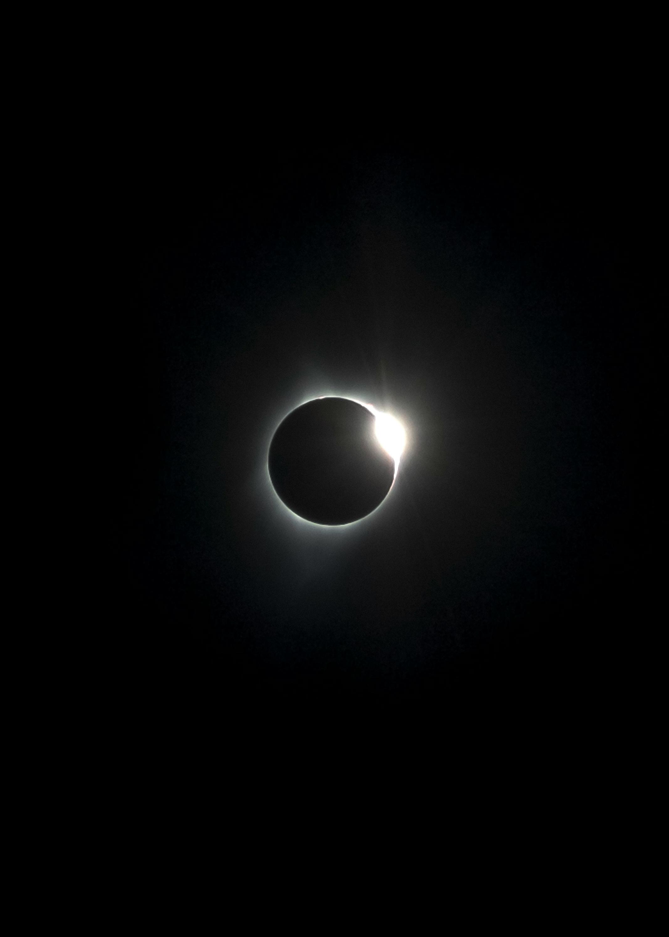 A total solar eclipse with the moon completely obscuring the sun, revealing bright pink solar flares along the sun's edge.