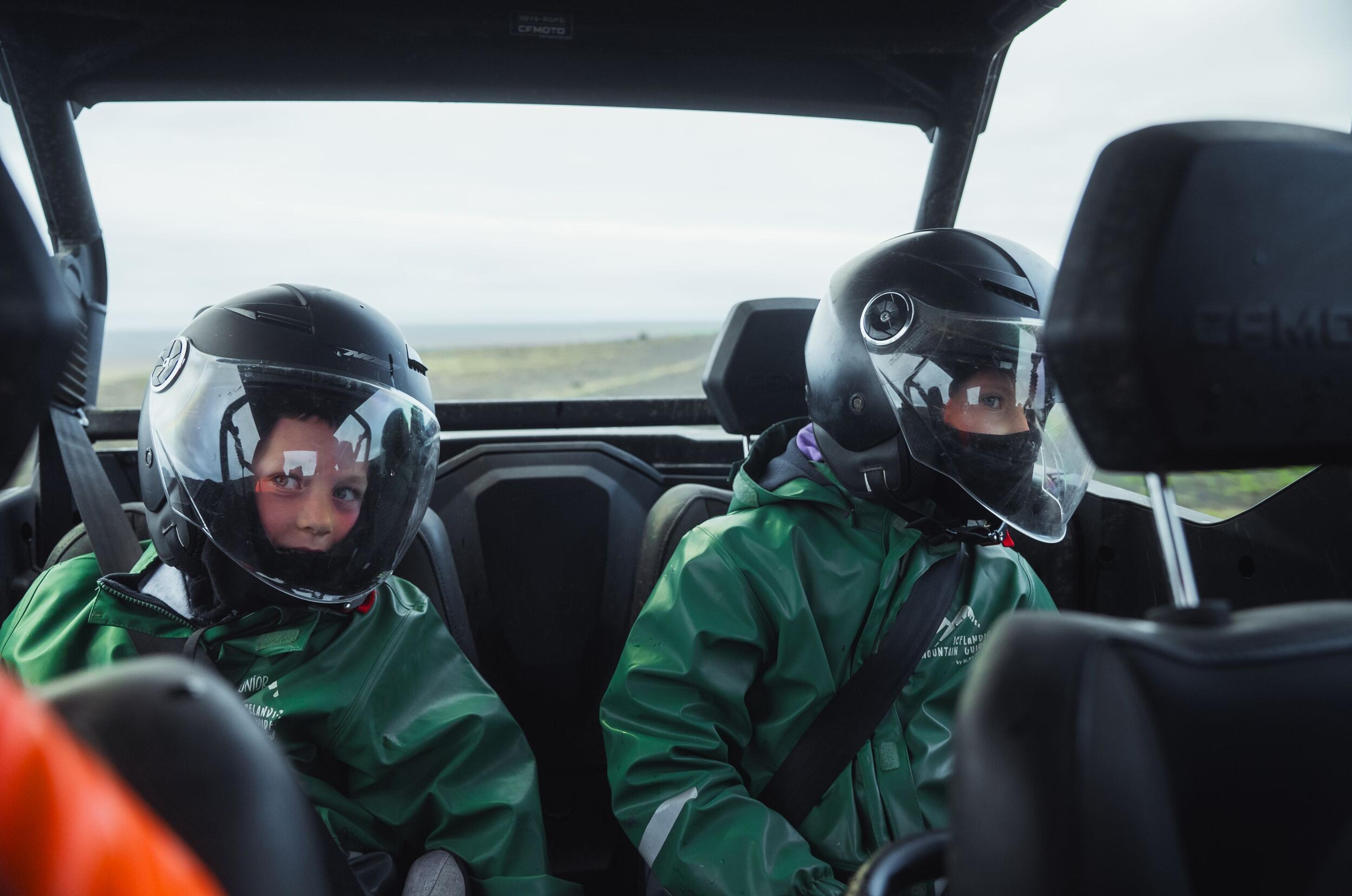 two people wearing helmets are sitting in the back seat of a vehicle .