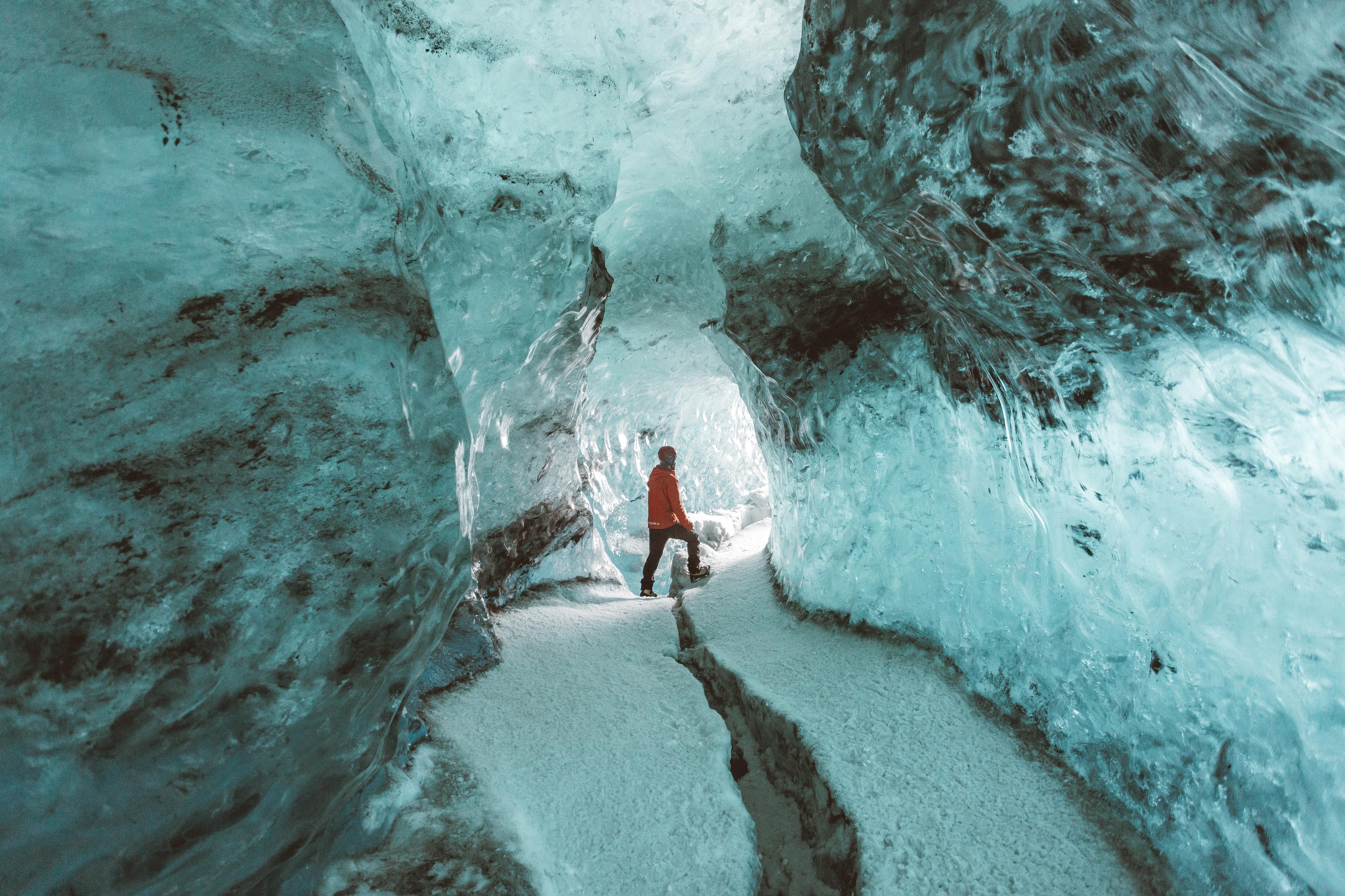 A person silhouetted against the luminous blue walls of an ice cave, emphasizing the vastness and ethereal beauty of the frozen cavern.