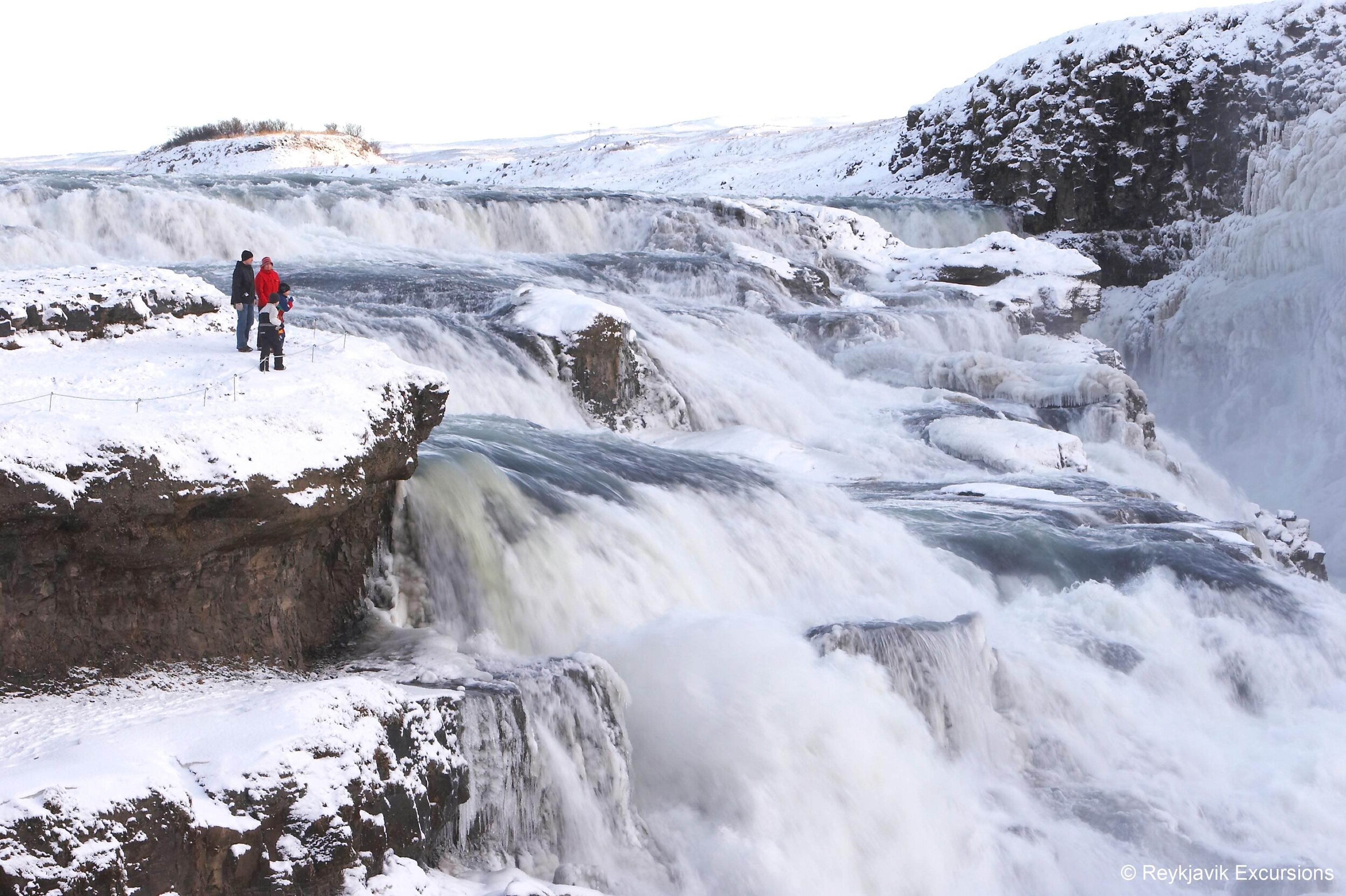 People admiring the Gullfoss Waterfall sorrounded by icy landscapes.