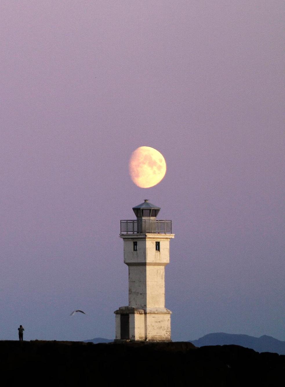 The two Akranes lighthouses in Iceland stand against a pastel twilight sky, with the moon rising between them, creating a serene coastal scene.