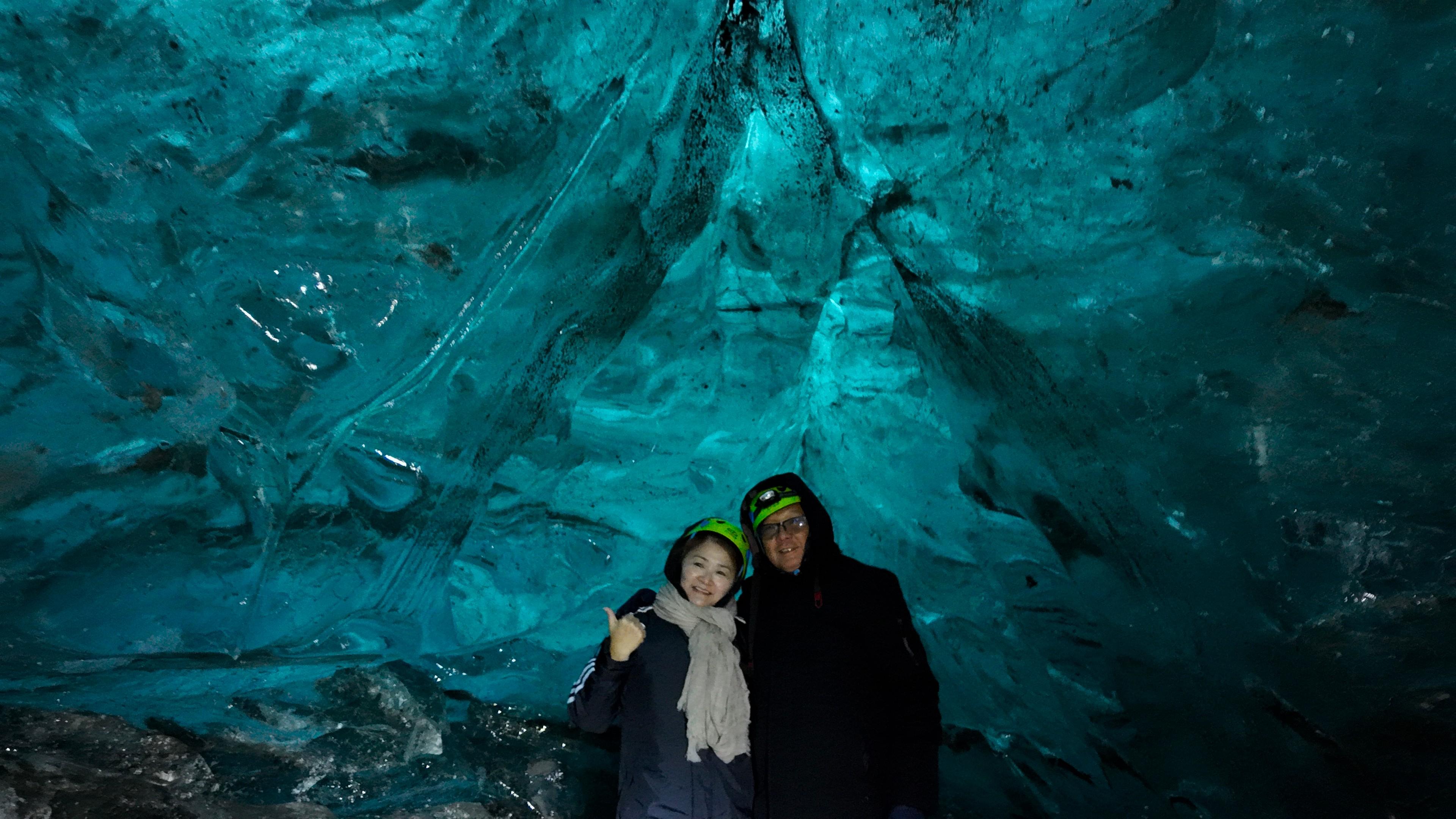 Two people in winter gear posing inside a blue-lit ice cave.