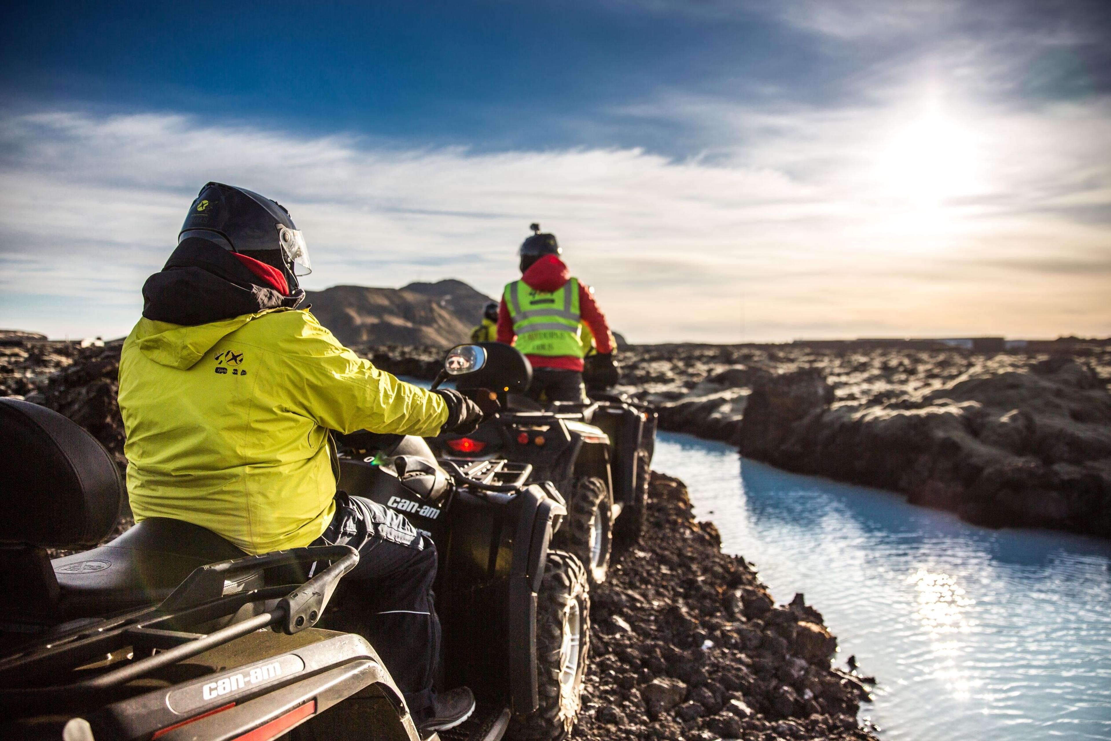 Two people driving ATV overlooking blue water in a lava fissure