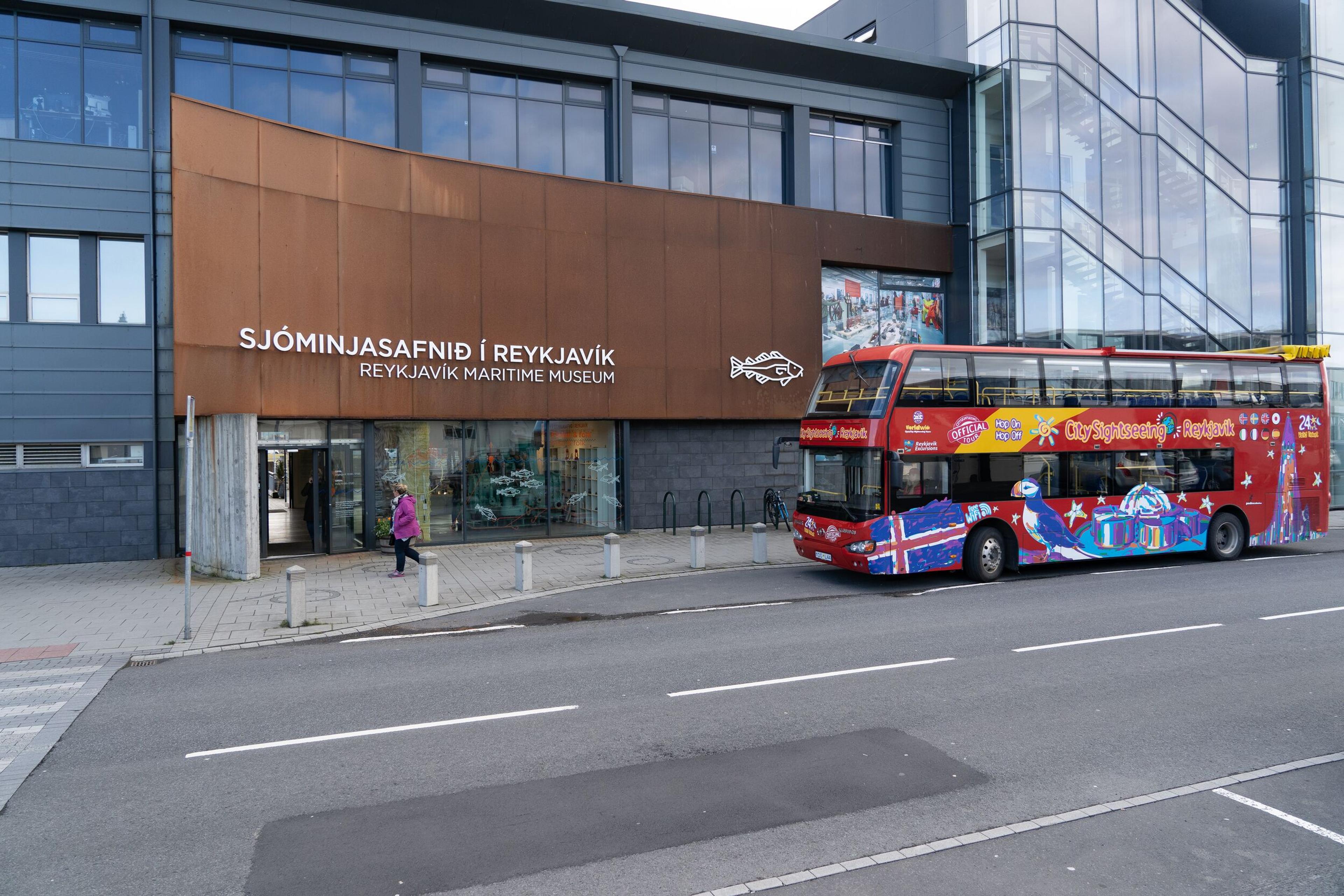 A colorful sightseeing bus parked by the entrance of the Reykjavik Maritime Museum with wooden decking and seating area.