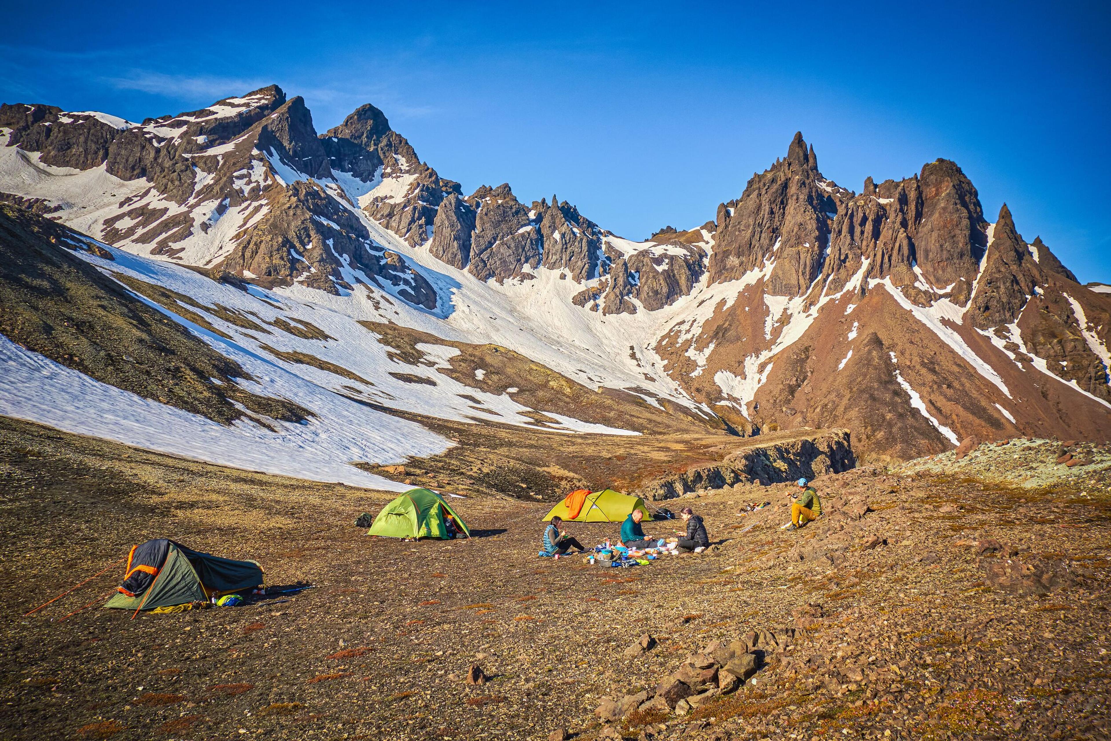 A campsite with tents and people in a rugged, snow-dusted mountain valley.