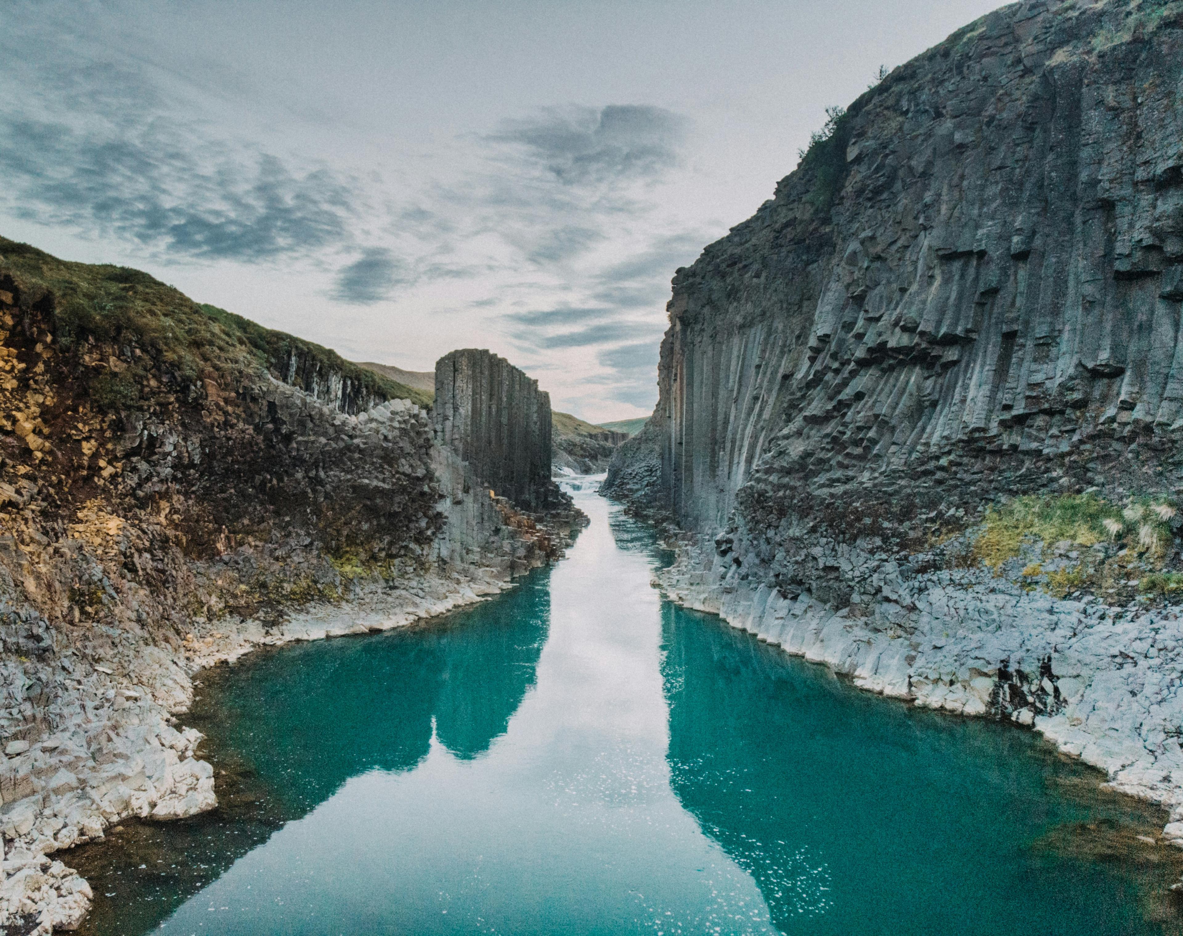 Turquoise river flowing through a canyon with dark columnar basalt cliffs under a cloudy sky.