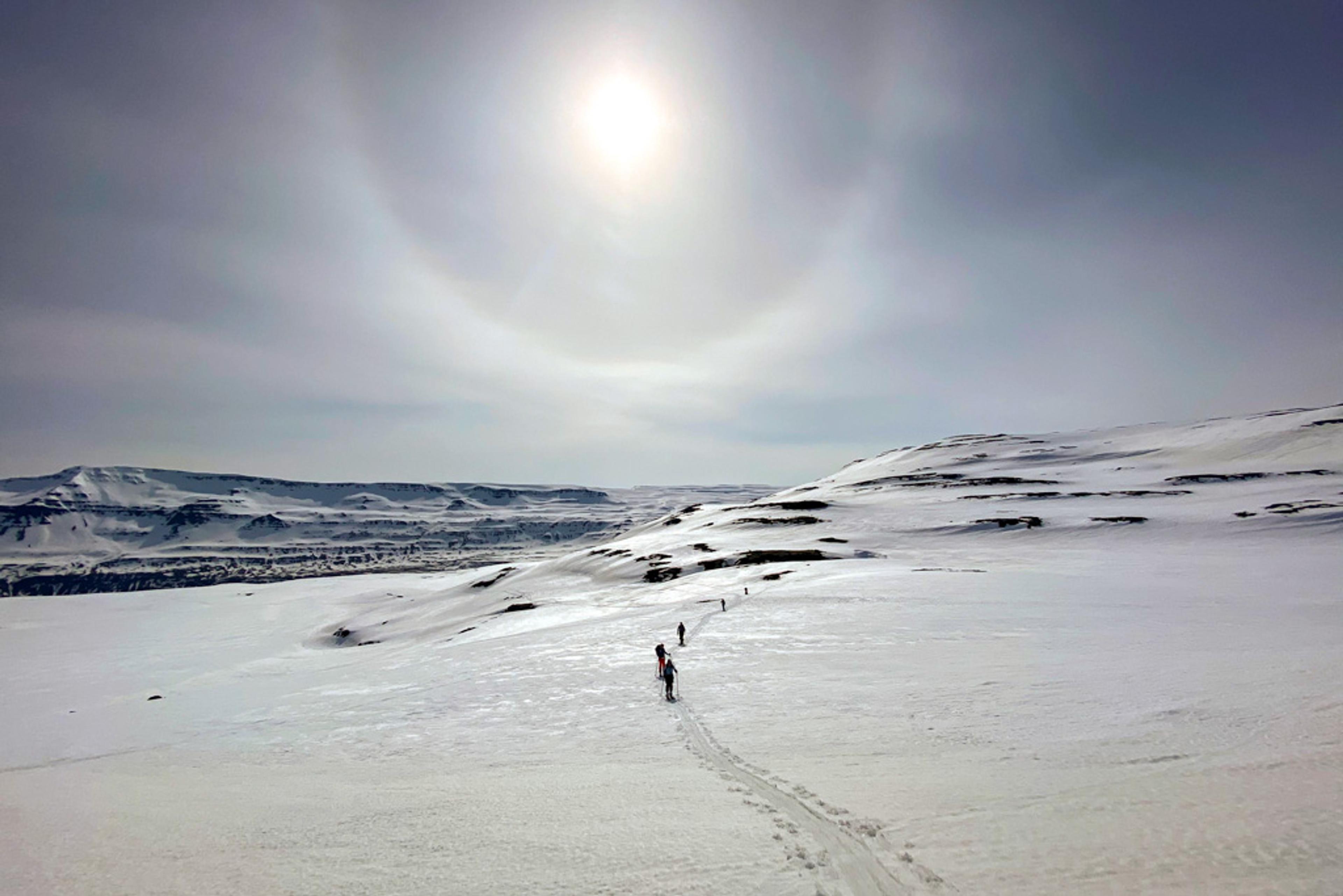Ski-tourers gracefully traversing a vast snowfield, bathed in radiant sunlight.