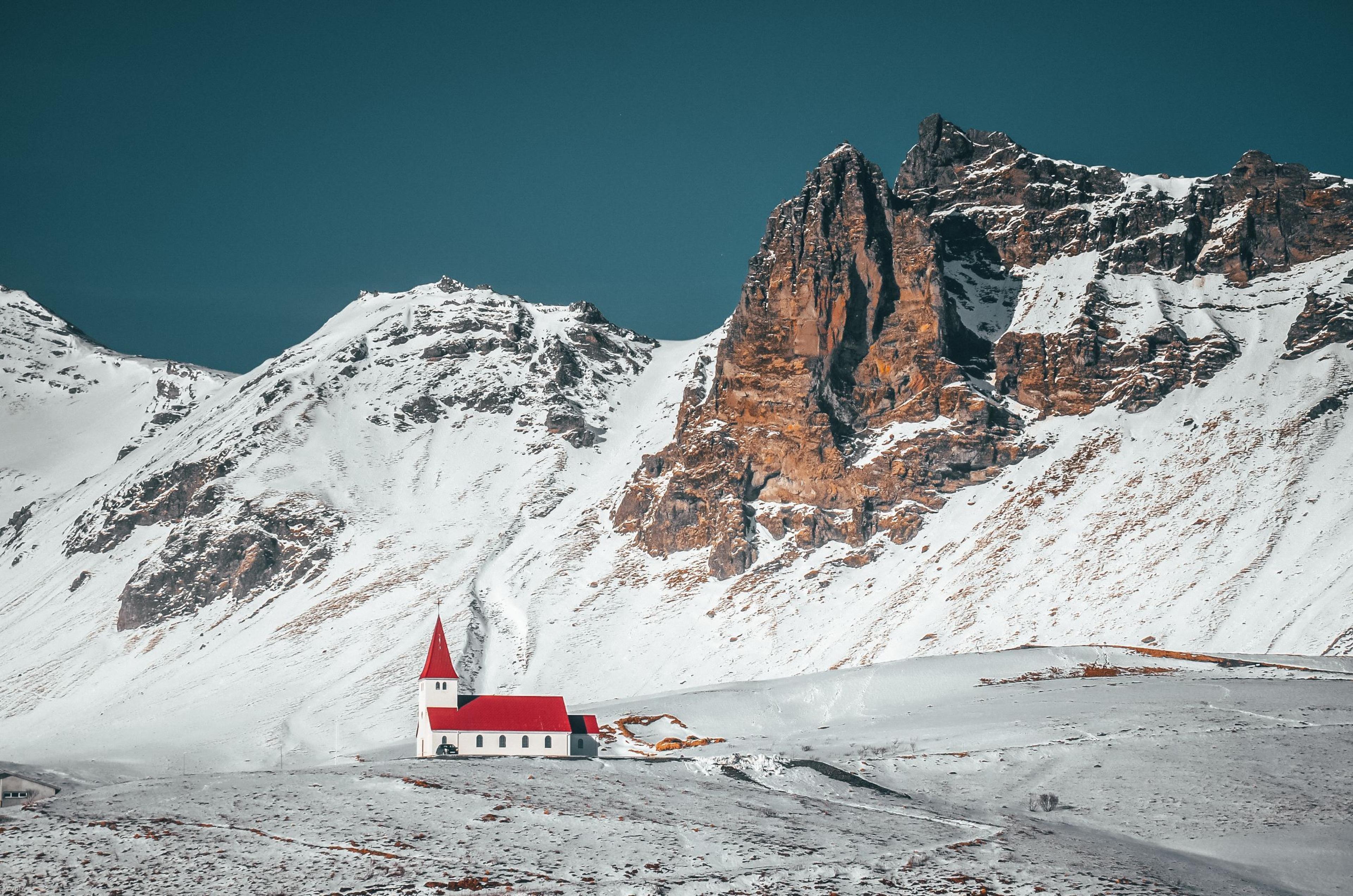 The red church of Vík during winter, set against a backdrop of brown mountains blanketed in snow.