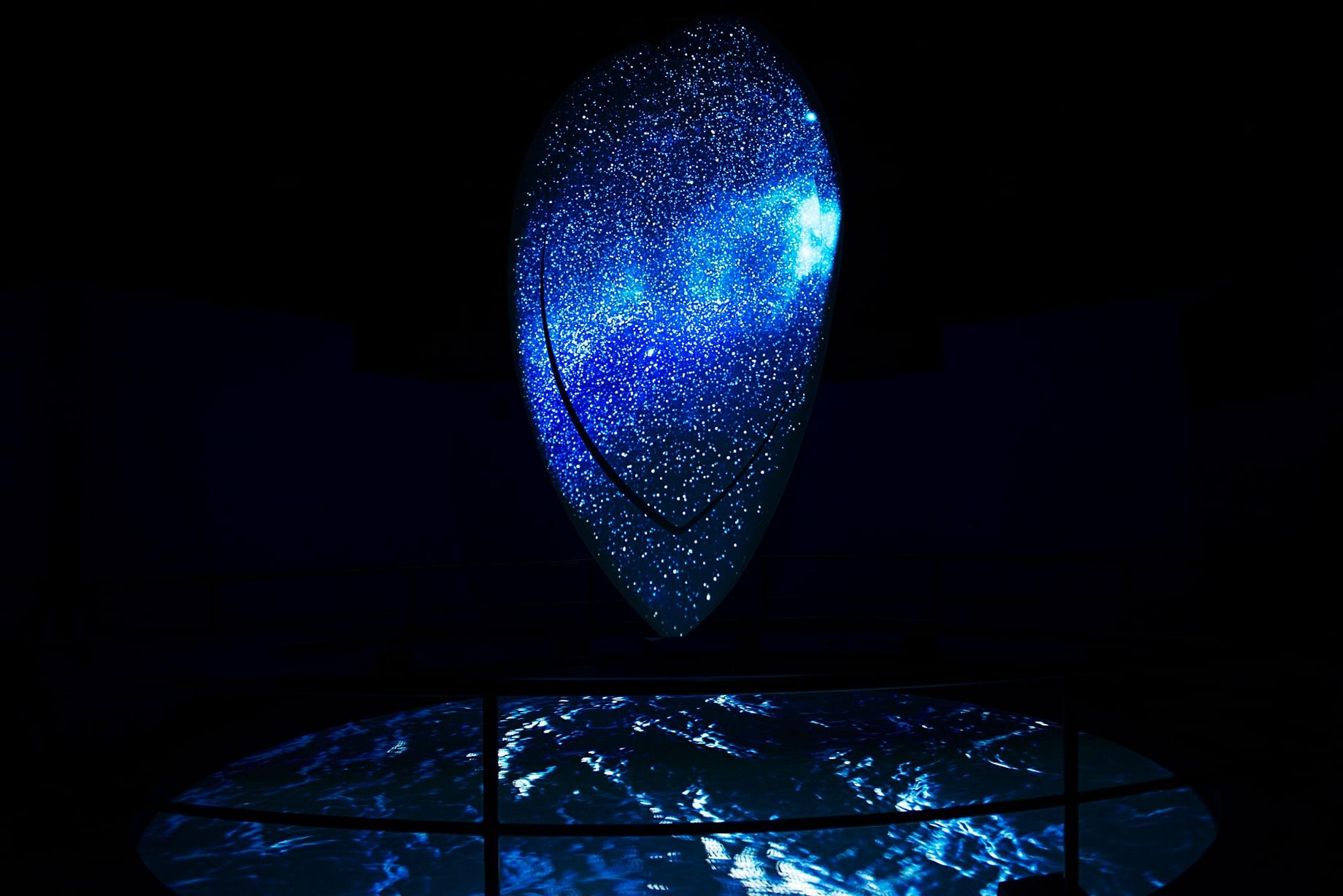 Abstract blue galaxy on a vertical screen, with blue waves on a curved floor display in a dark room.