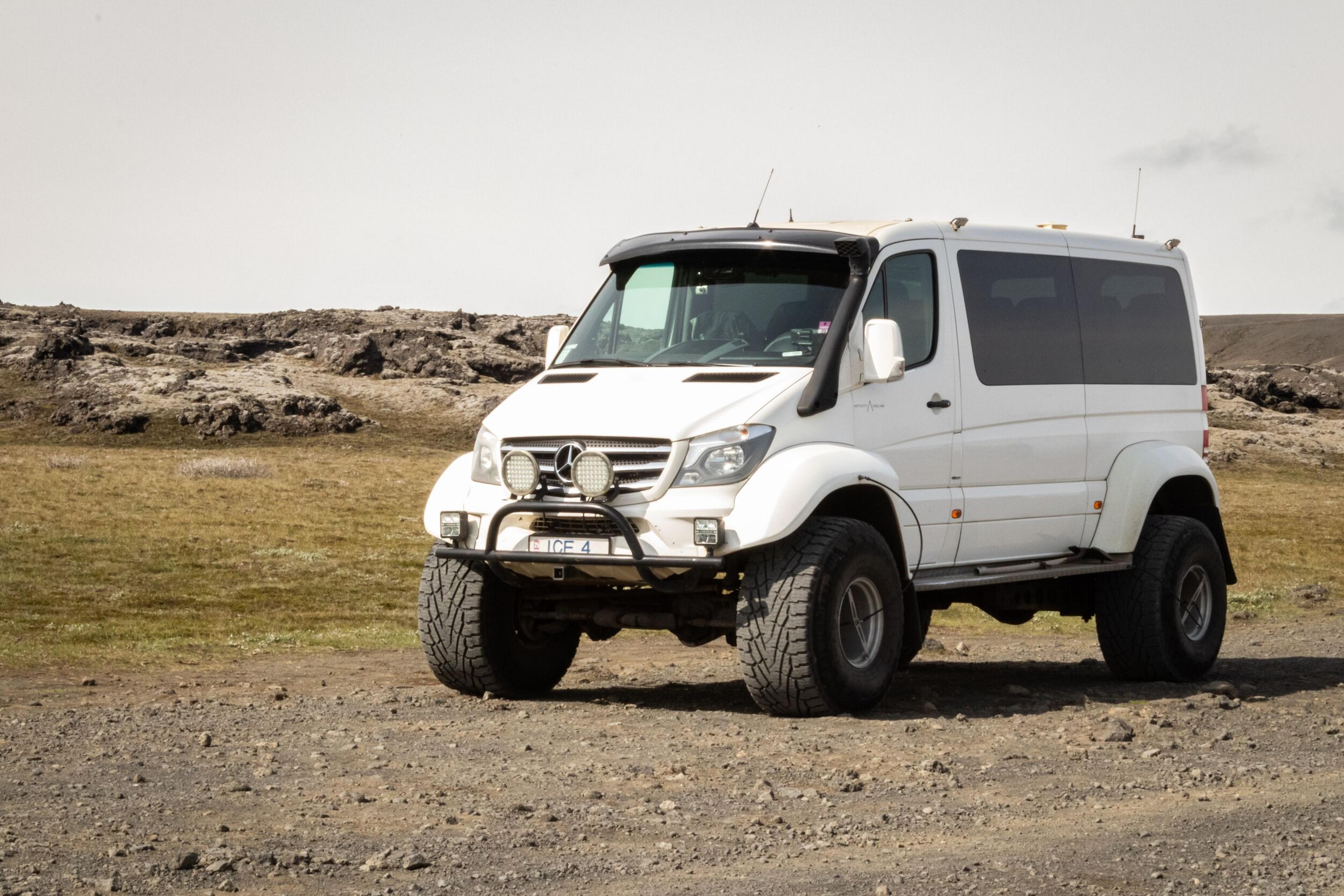 White off-road 4x4 vehicle with large tires and front grille, parked on a dirt path surrounded by Iceland's rugged landscape.