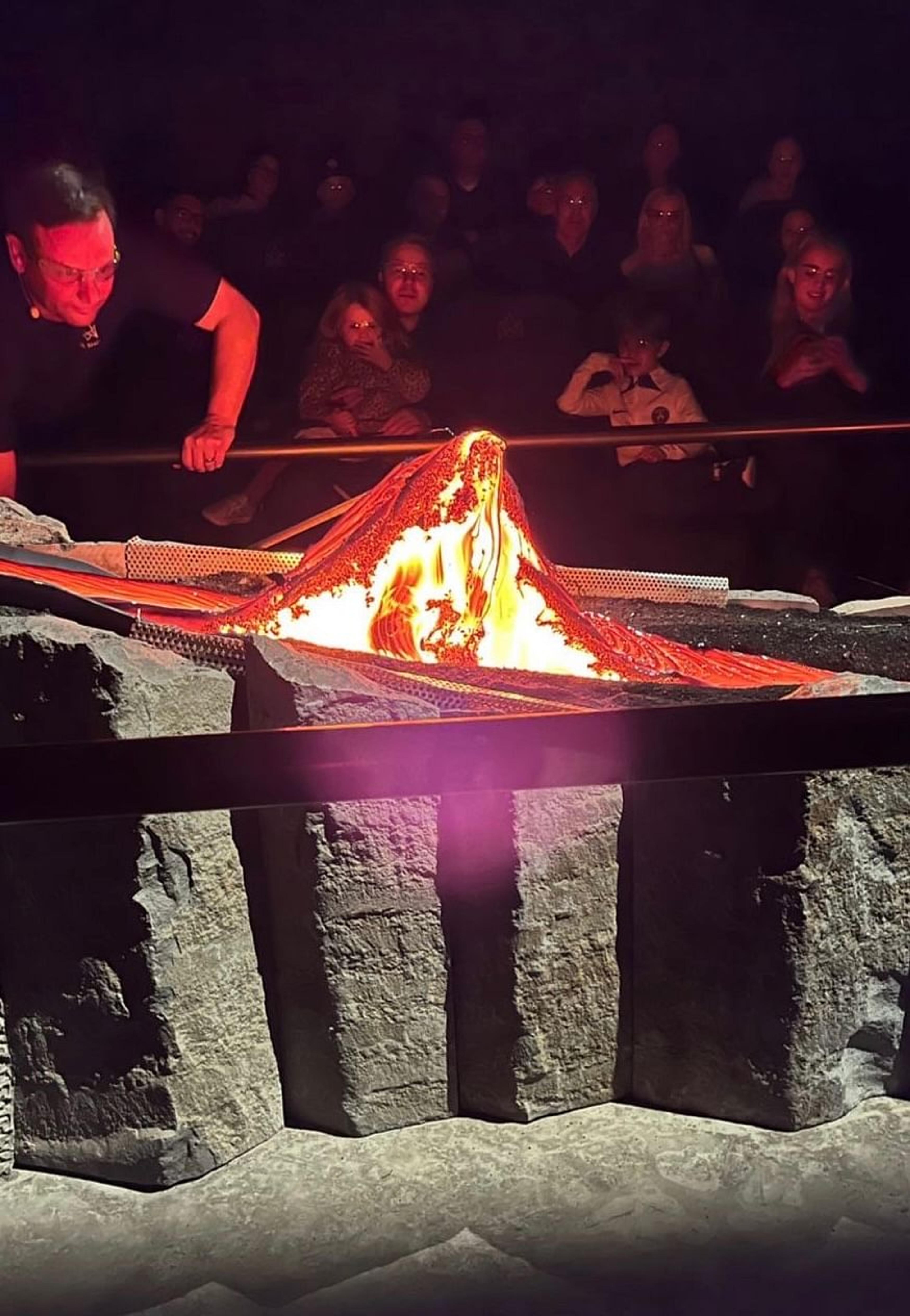 A man demonstrates a simulated volcanic eruption with glowing "lava" to a dark audience.
