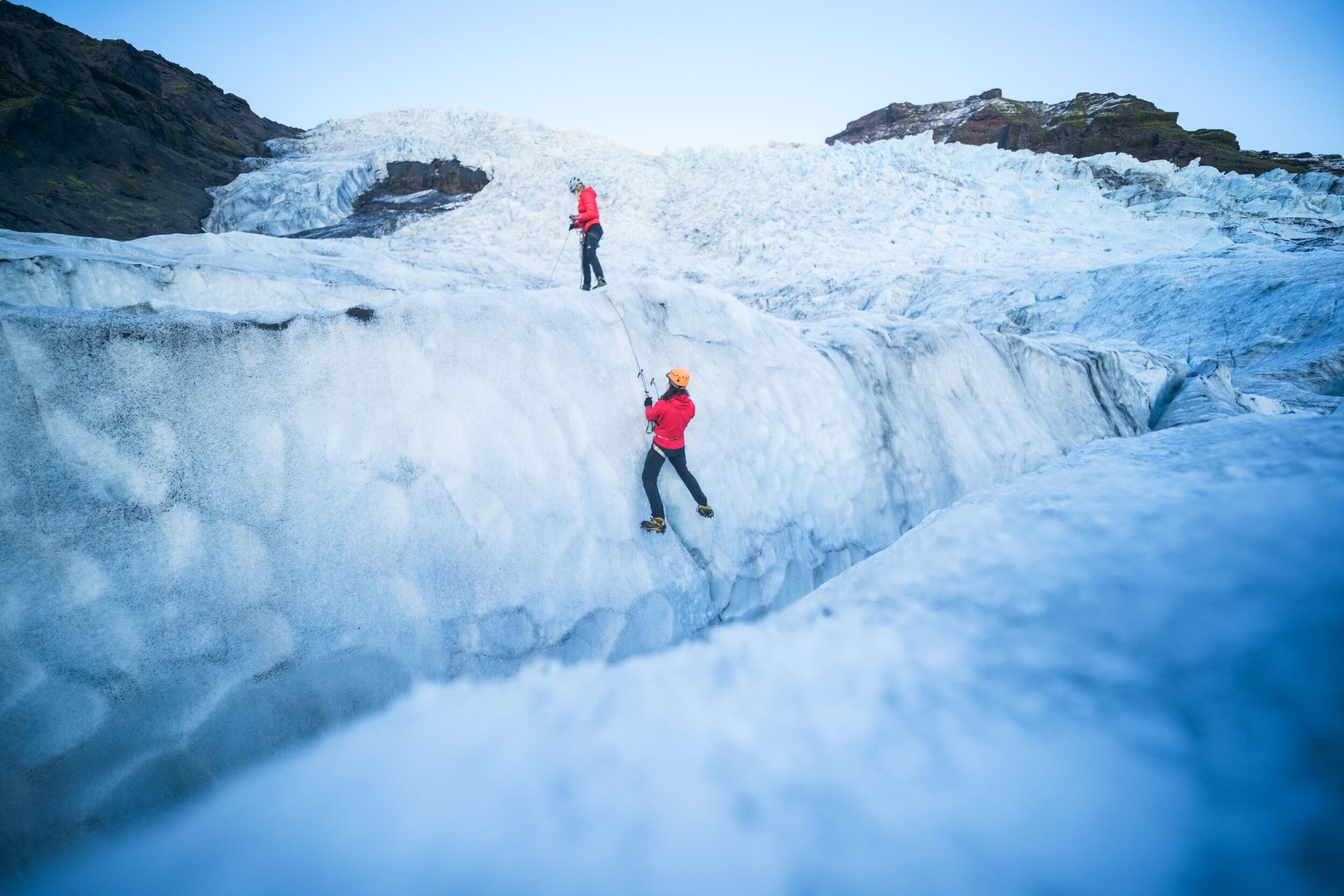 Two explorers climbing an ice wall on a glacier in Iceland.