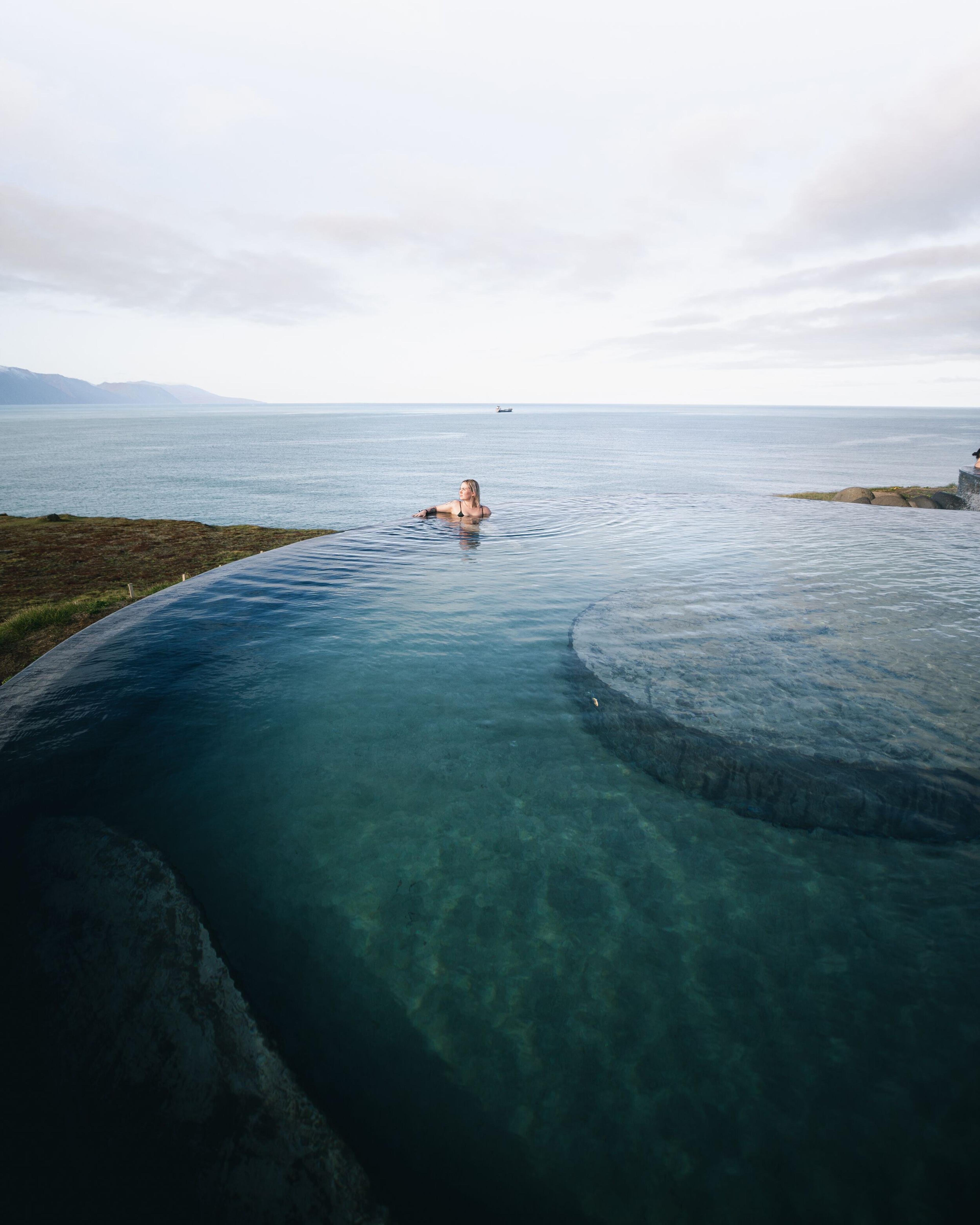 a woman is swimming in an infinity pool overlooking the ocean .