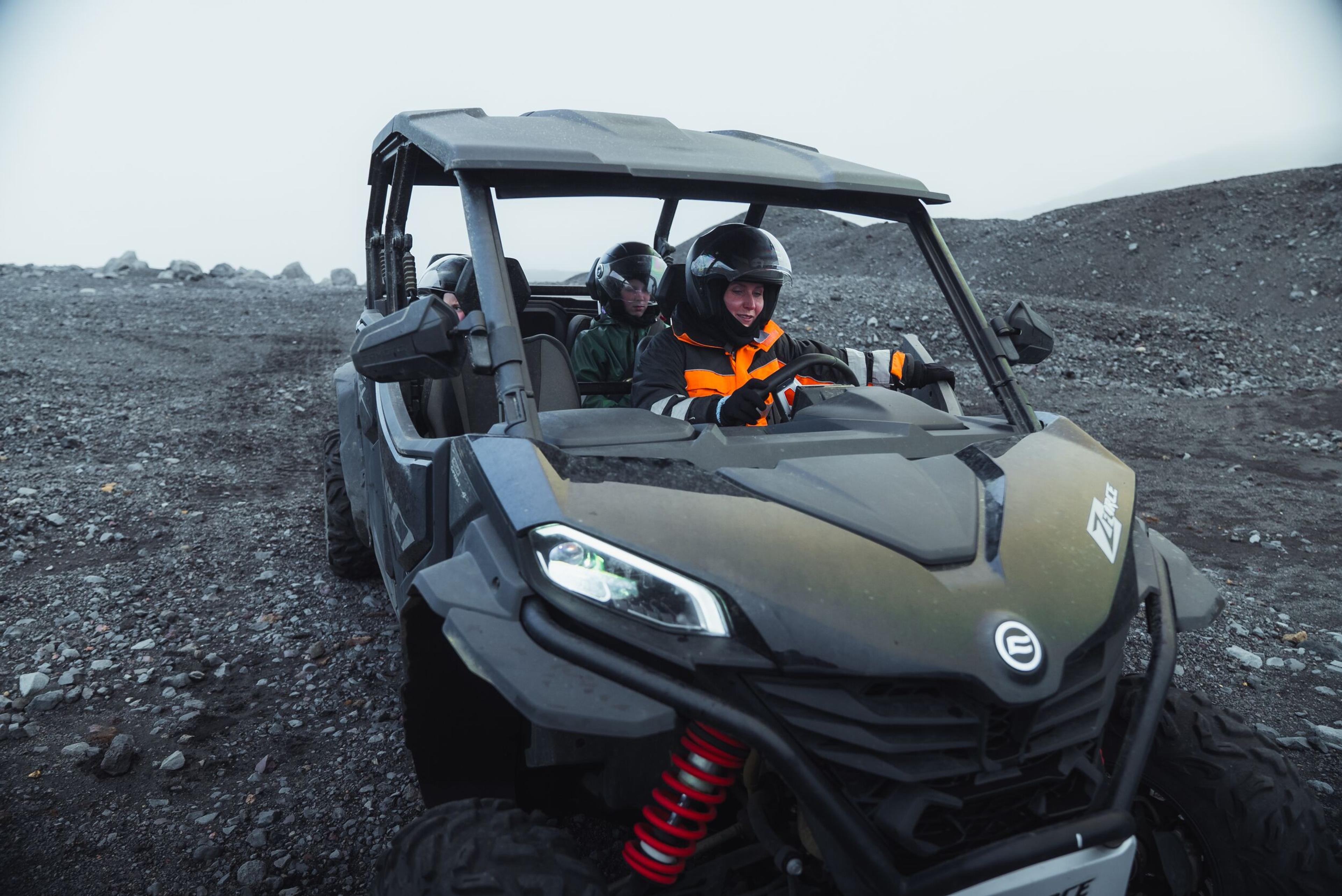 Two people wearing helmets drive a UTV on a rocky, desolate landscape.
