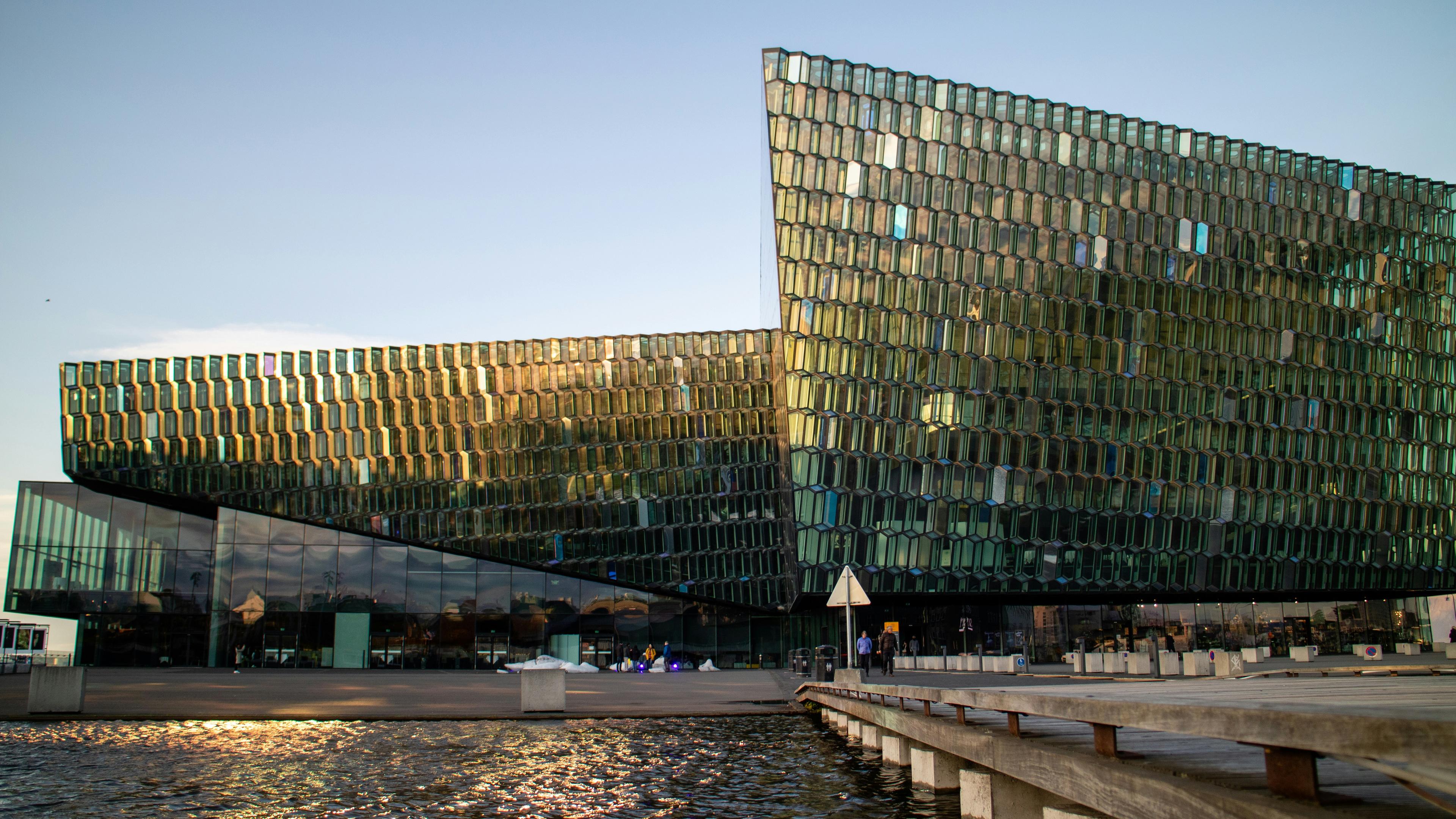 Modern glass building of harpa in Reykjavík reflecting sunlight by a waterfront.