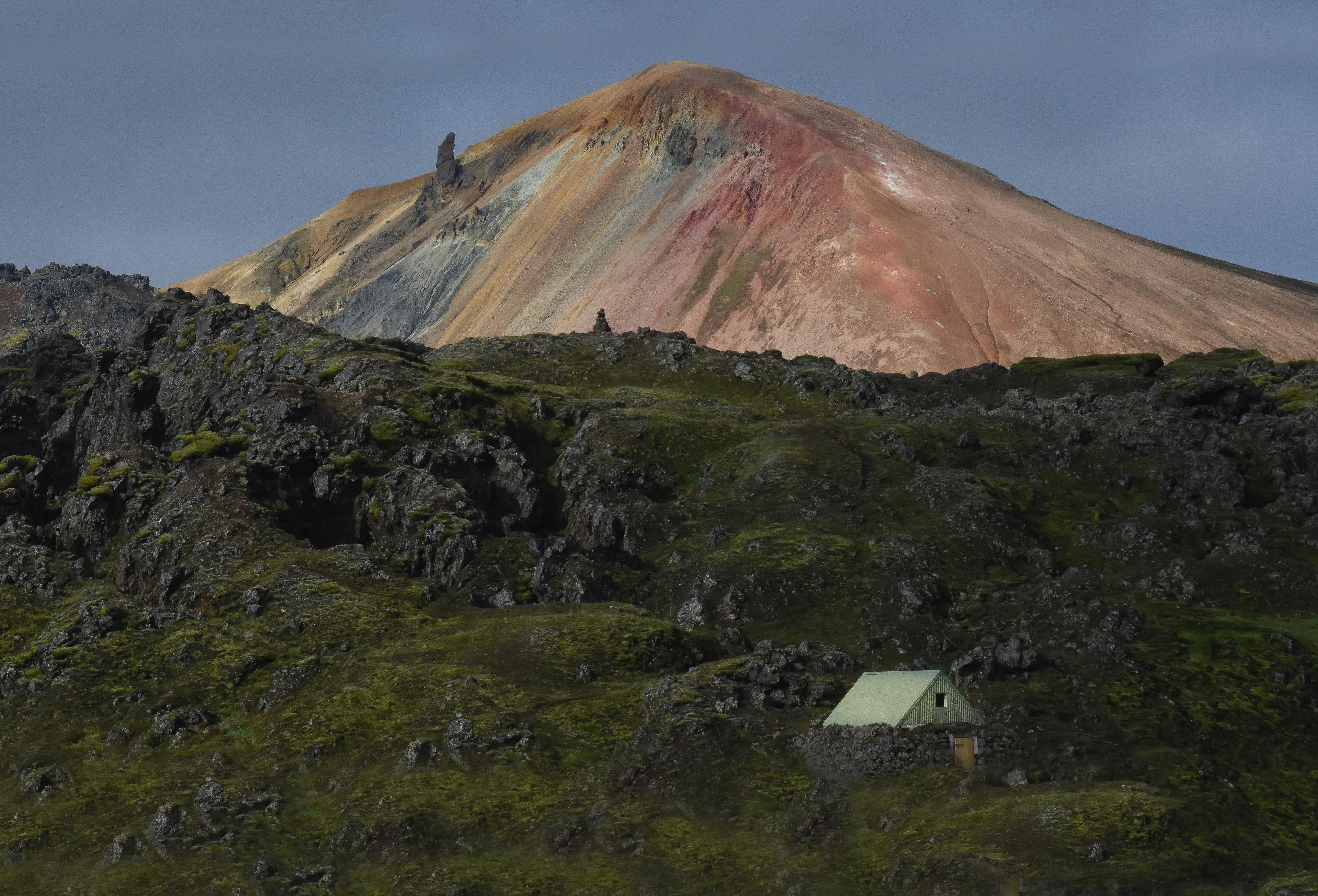 A small tent is set up on lush green terrain with the colorful, volcanic peak of Brennisteinsalda, Landmannalaugar, in the background.