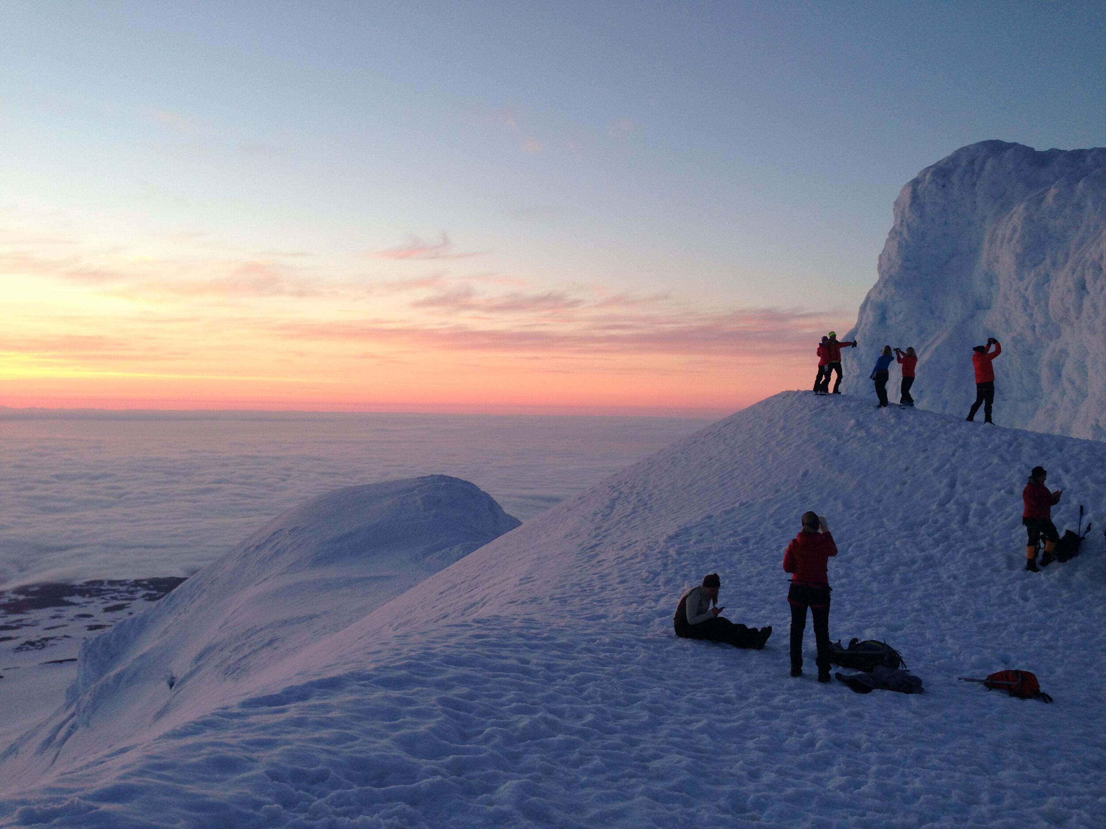 Group of hikers taking pictures on their hike to the Snæfellsjökull glacier summit. Sunset on the background.