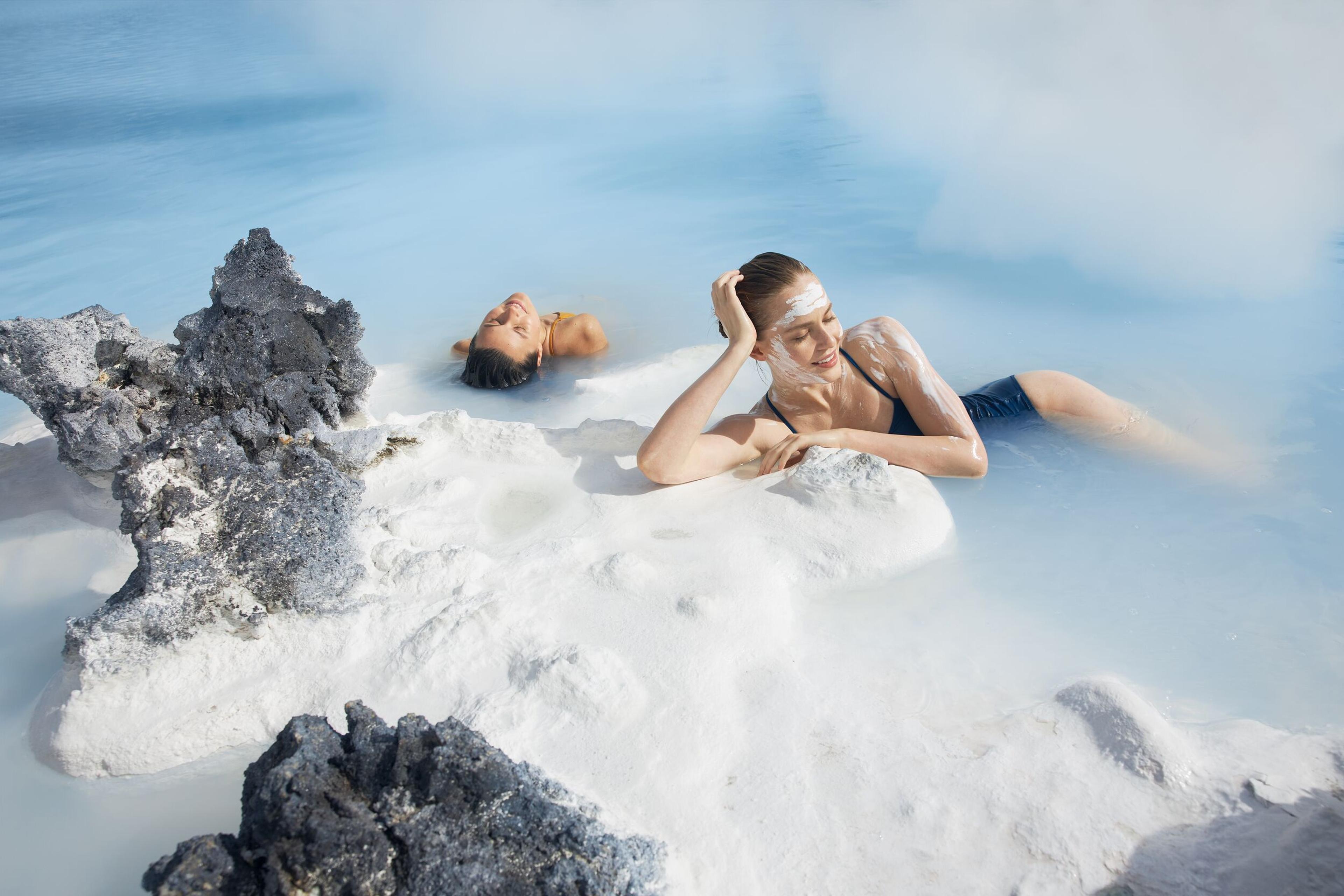 A woman reclining peacefully on a white rock amidst the serene waters of the Blue Lagoon.