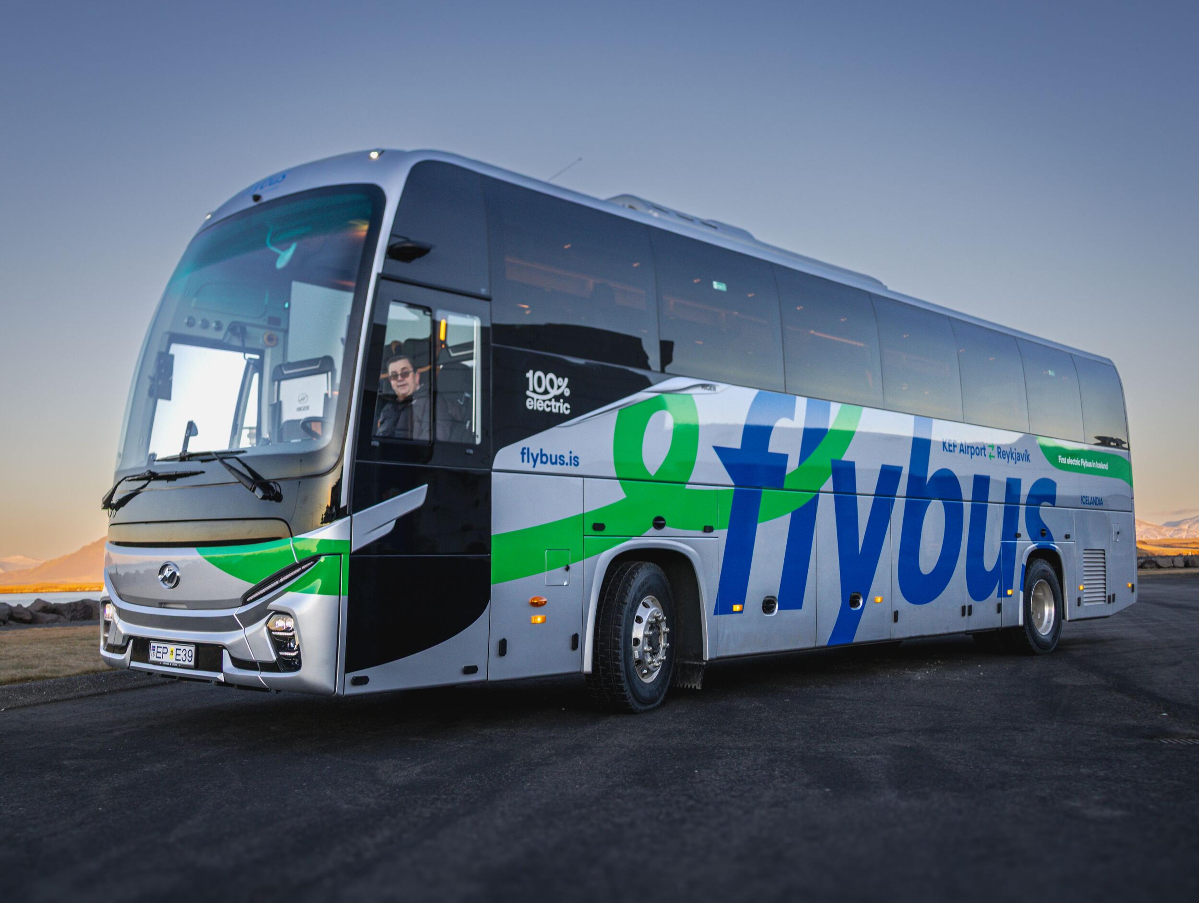 A silver electric Flybus coach with green and blue branding, with a driver visible inside.
