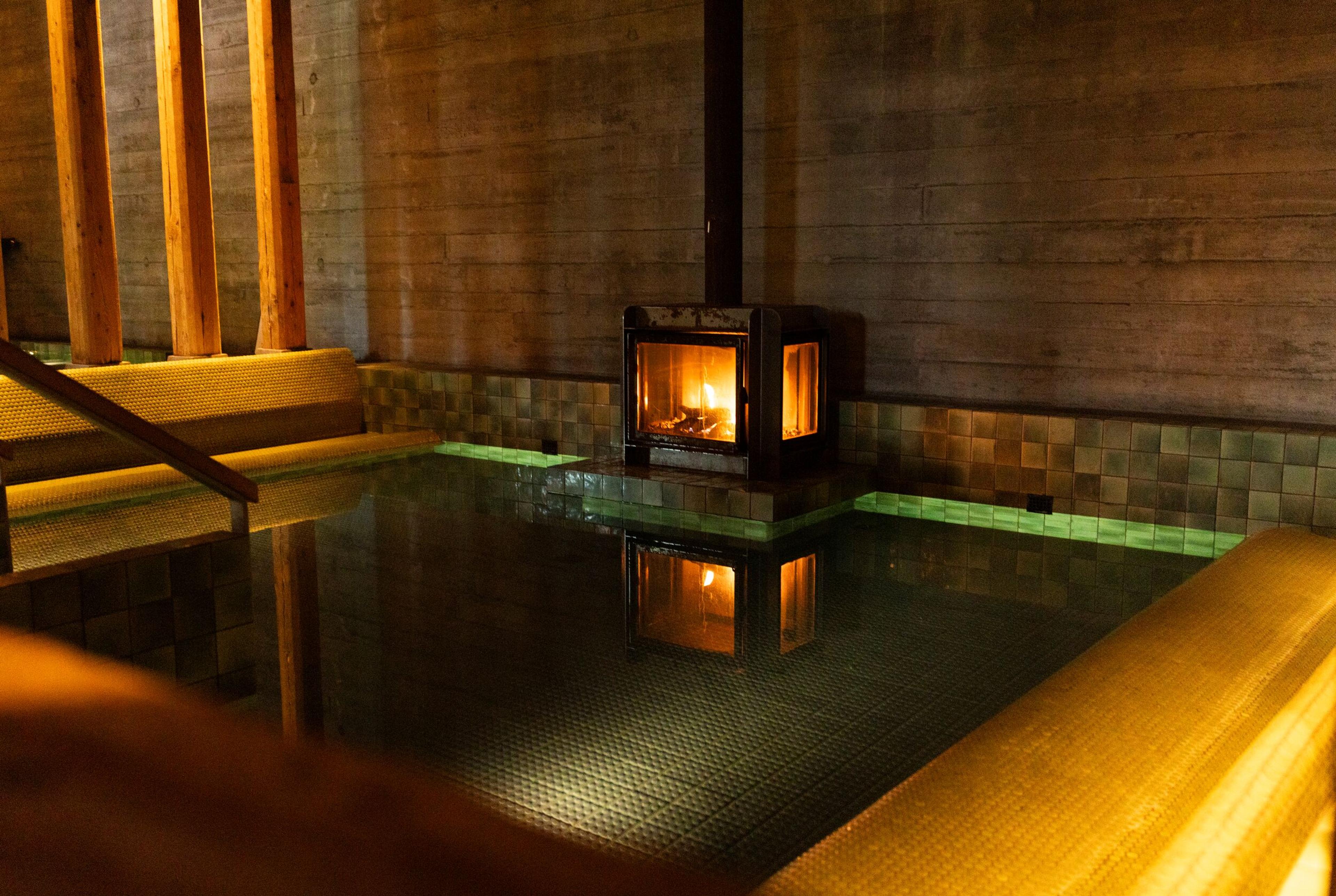 Indoor pool with a lit fireplace reflecting in the water.