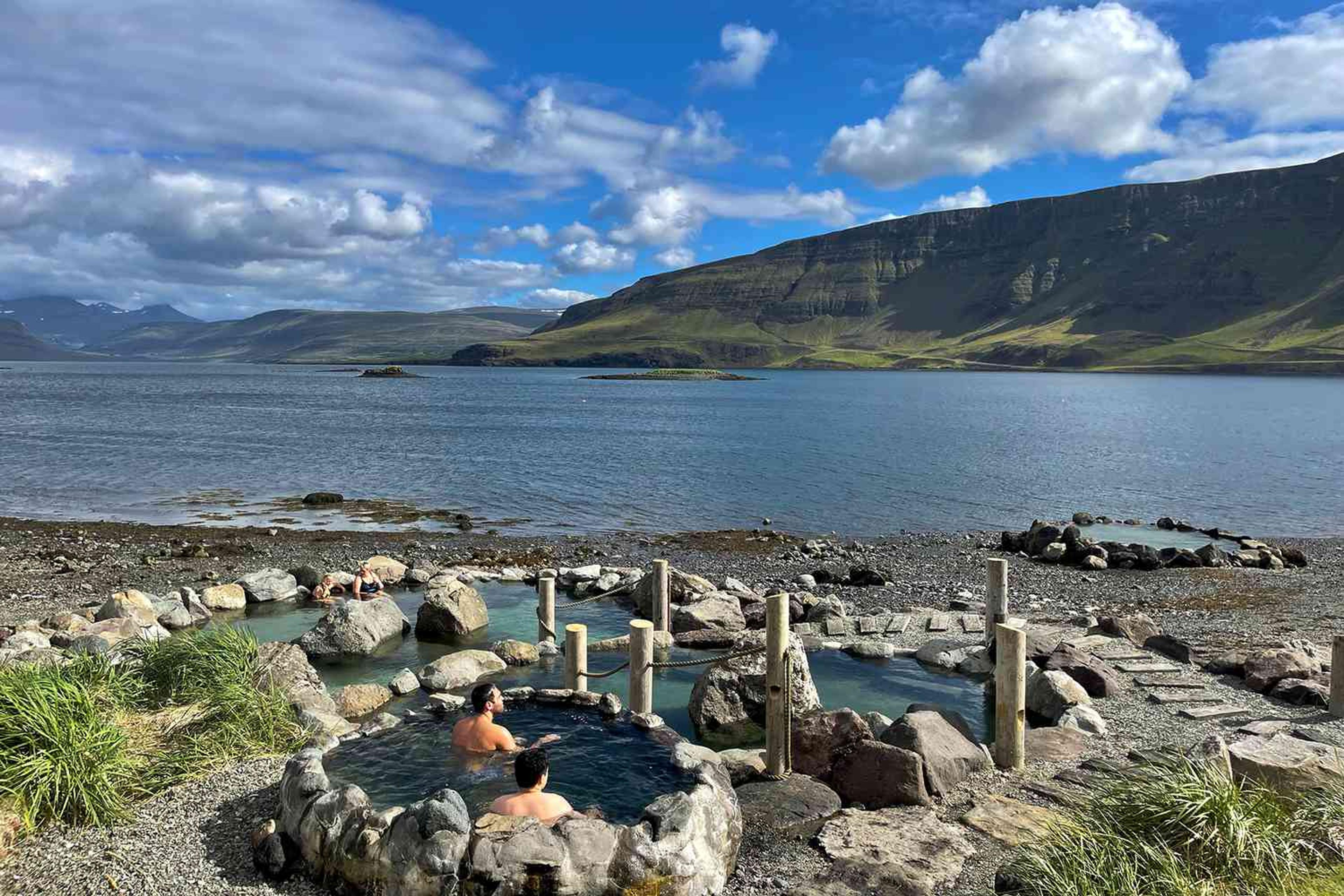 Two individuals enjoying the authentic warmth of Hvammsvík hot springs, nestled along the edge of a scenic fjord.