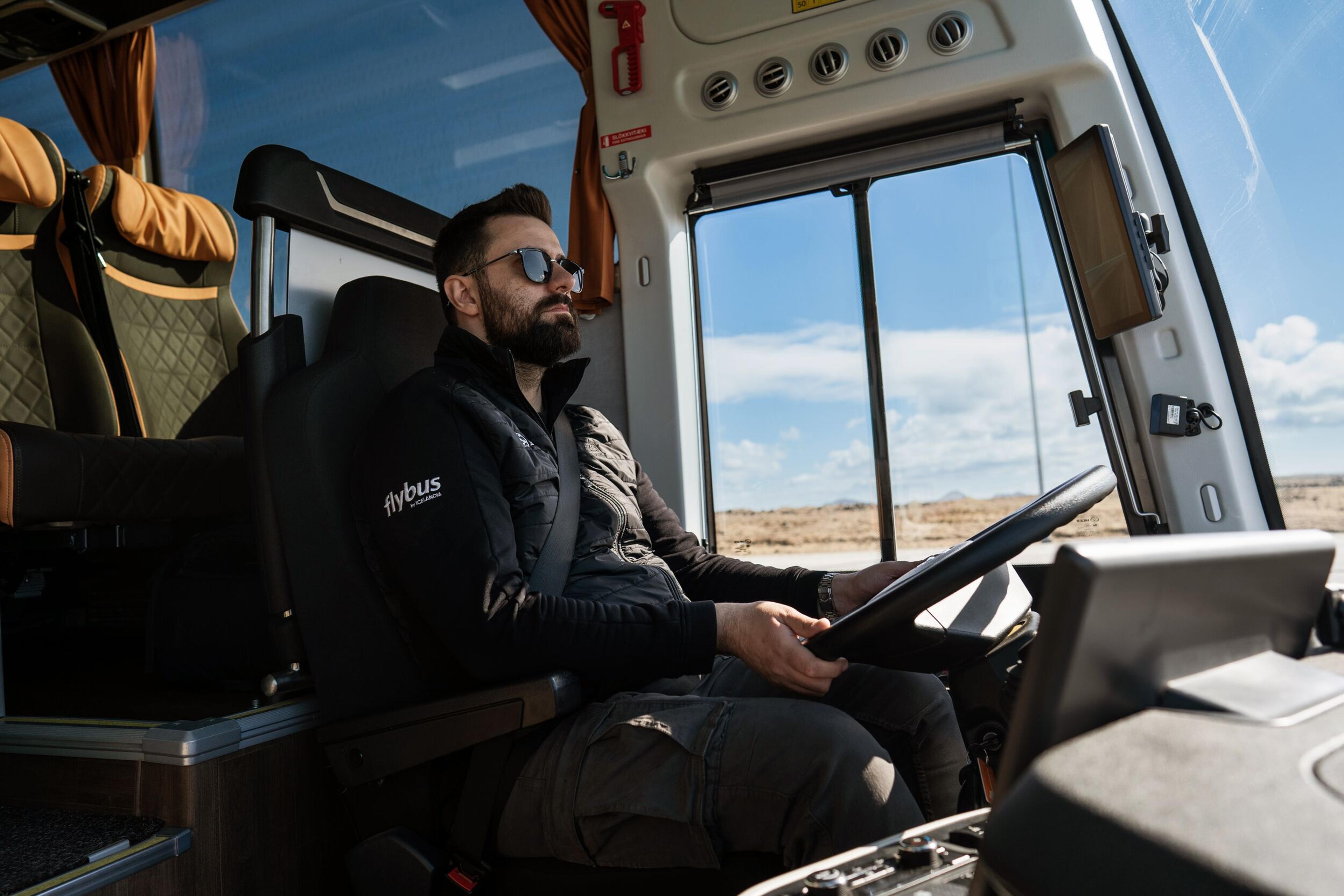 A bus driver, focused and driving, with a dashboard view from the passenger's perspective.