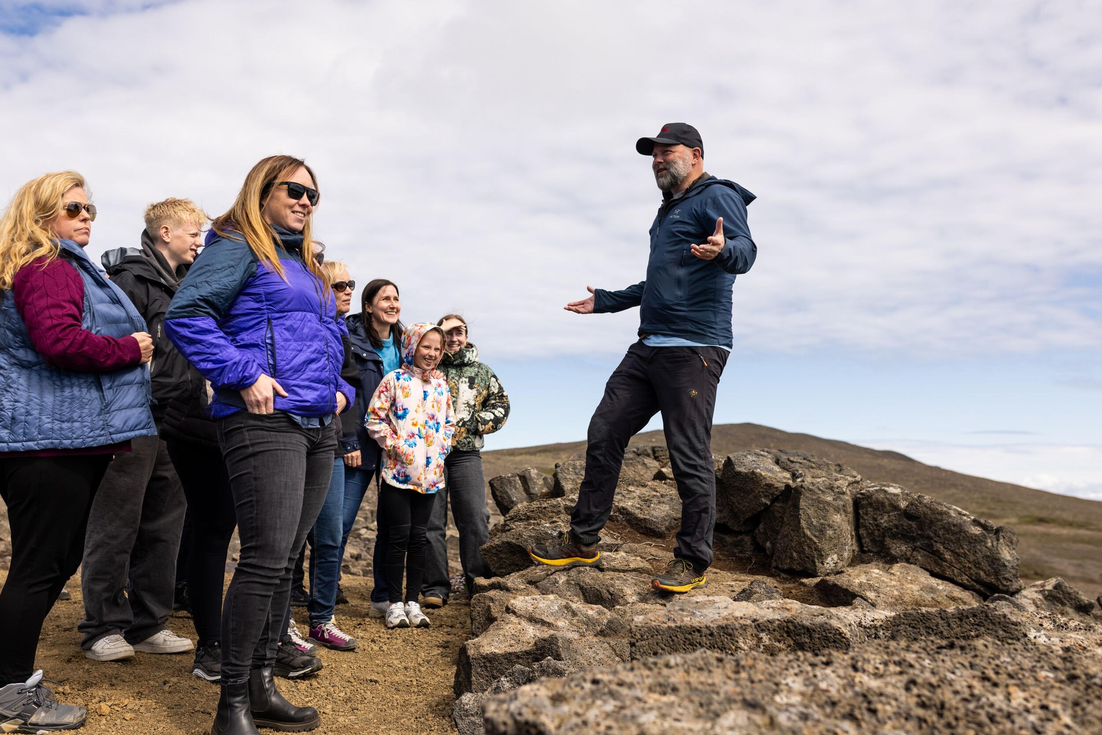 a man is standing on top of a rocky hill talking to a group of people .