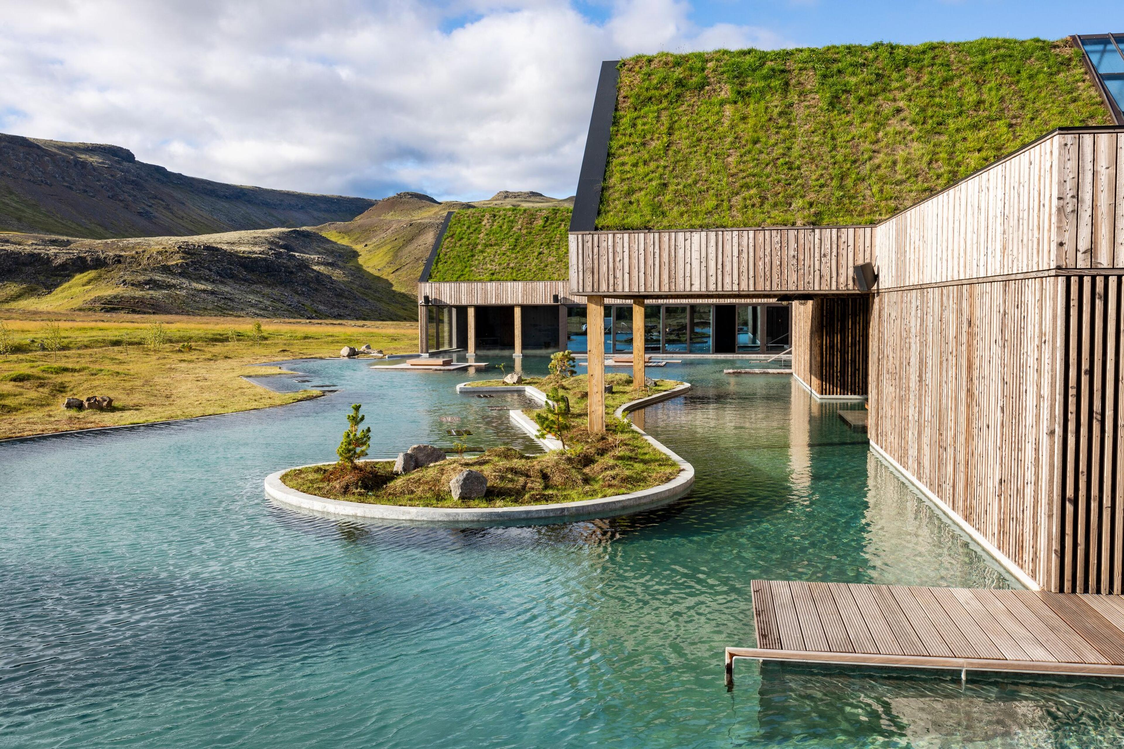 Geothermal spa with green-roofed wooden buildings and winding blue pools in a mountain valley.