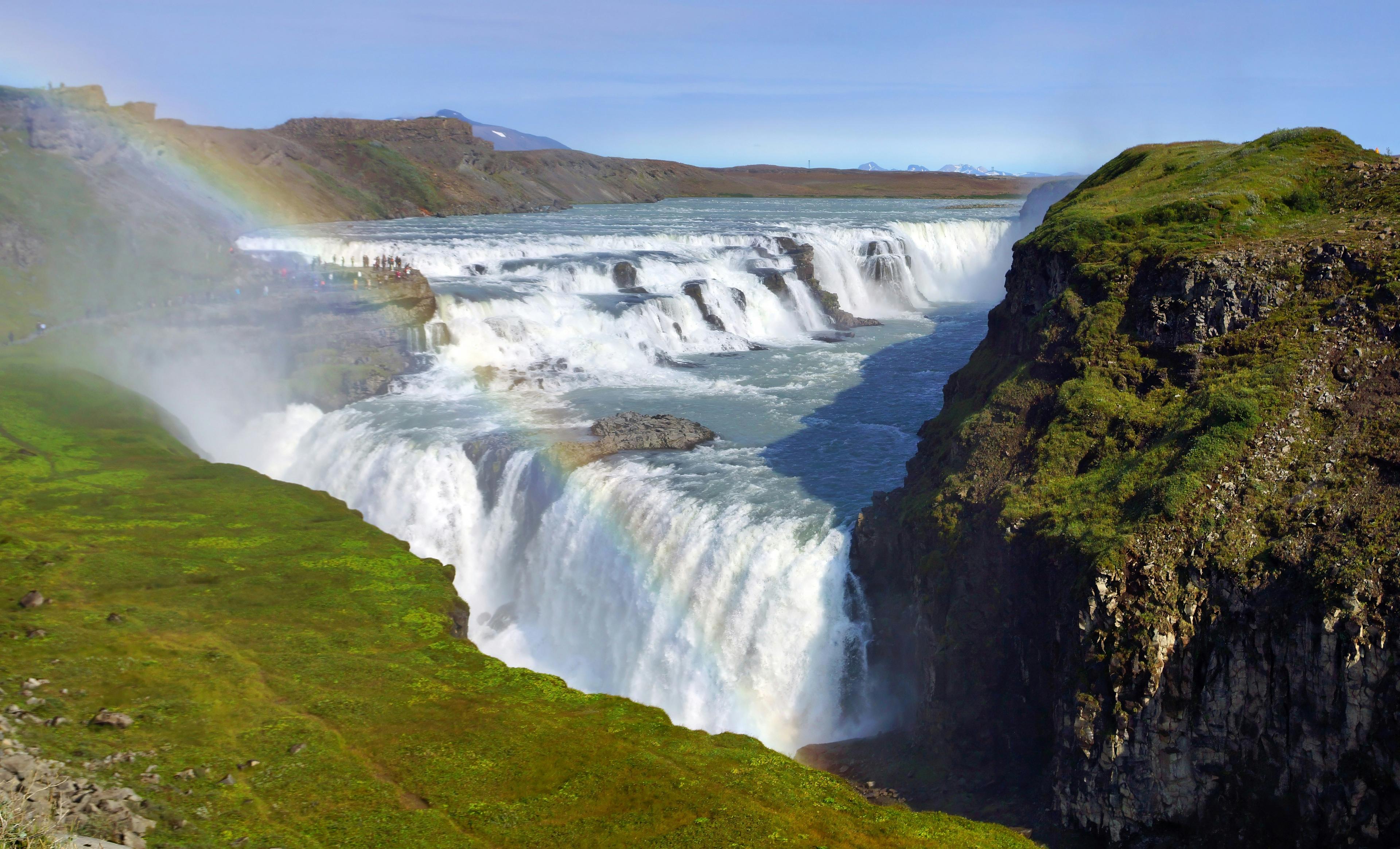 Gullfoss waterfall in Iceland, with lush green surroundings and a vibrant rainbow arching through the mist.