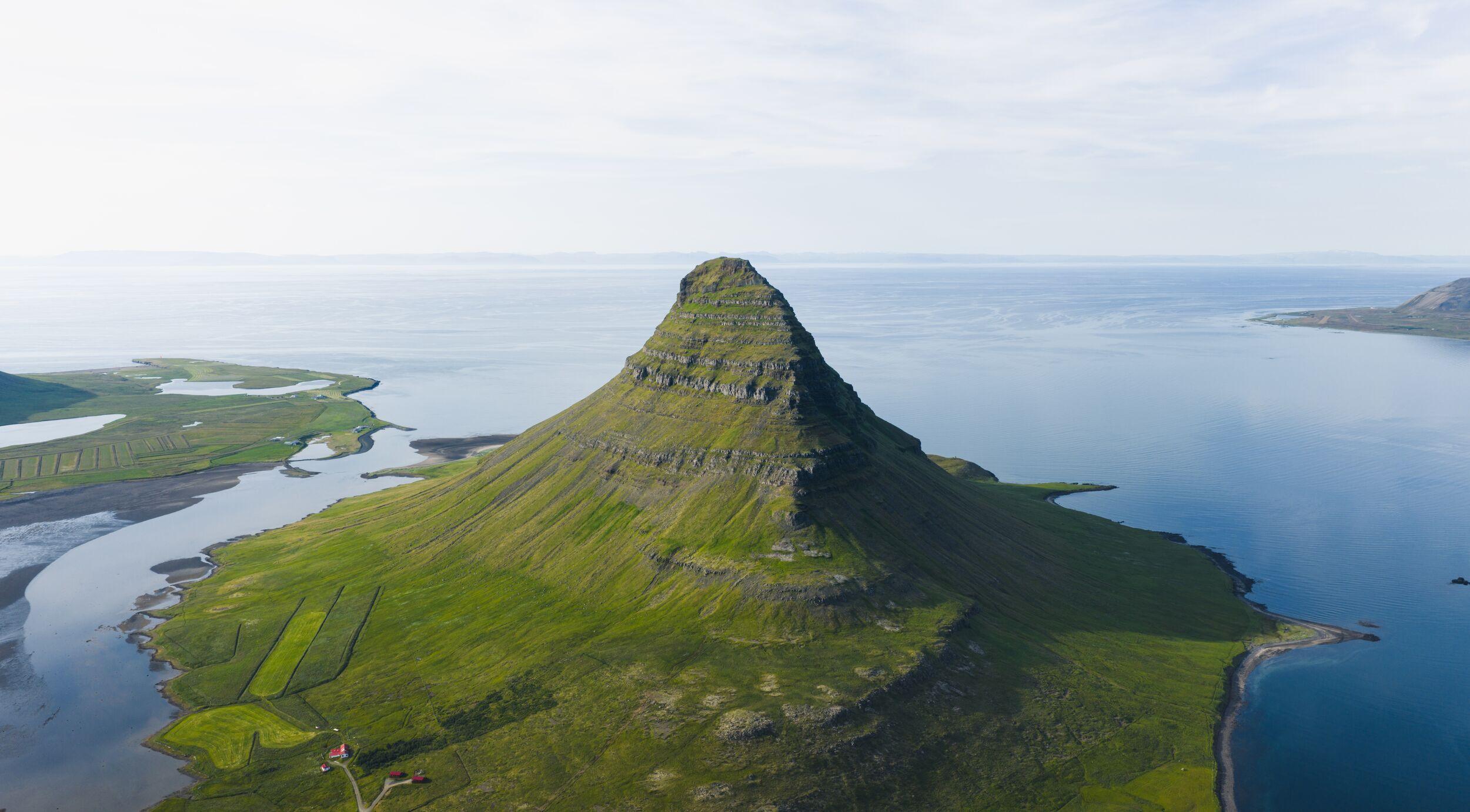 A green, conical mountain rising from a calm blue fjord.