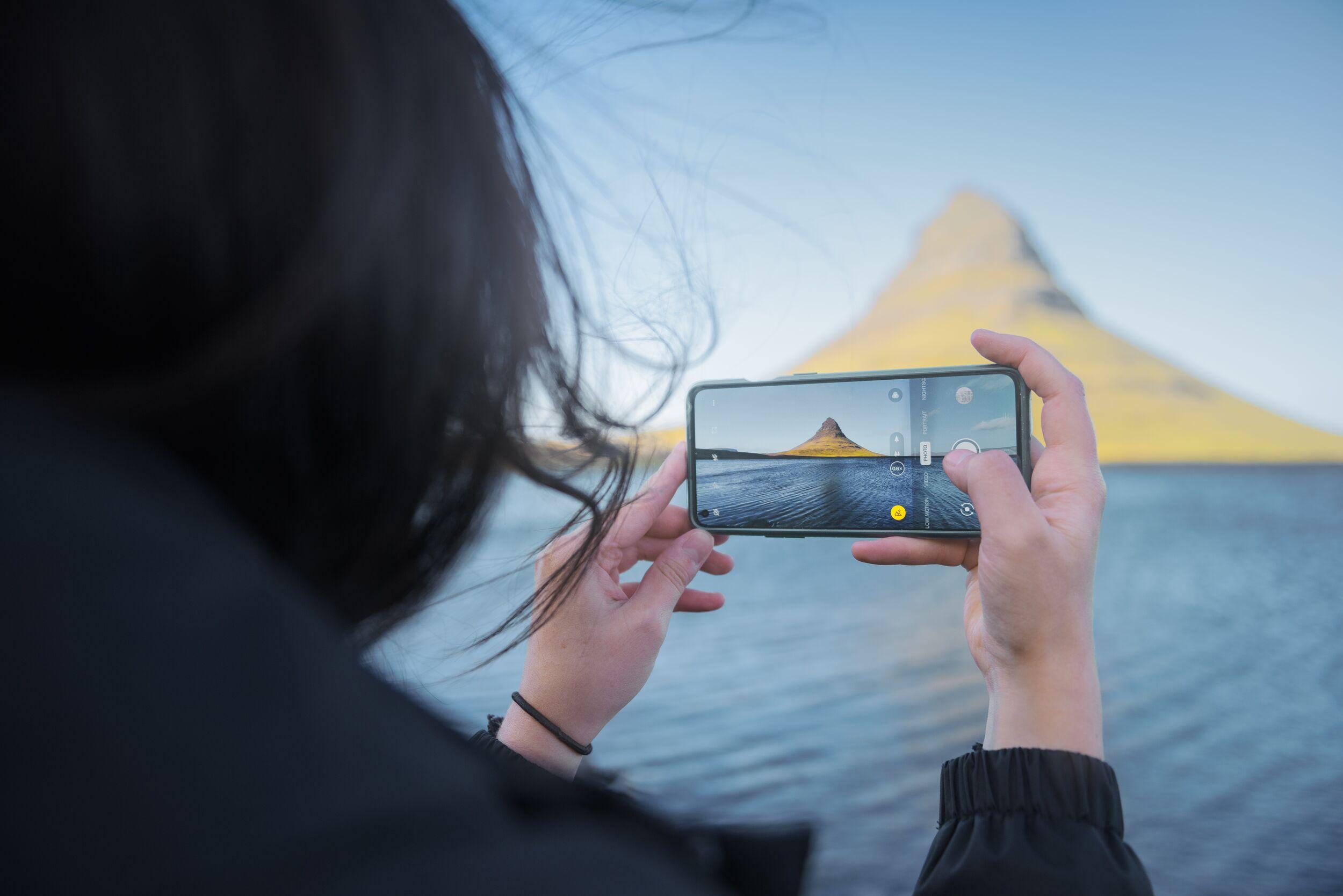 A person taking a picture with a phone of the Kirkjufell Mountain in the Snæfellsnes peninsula.