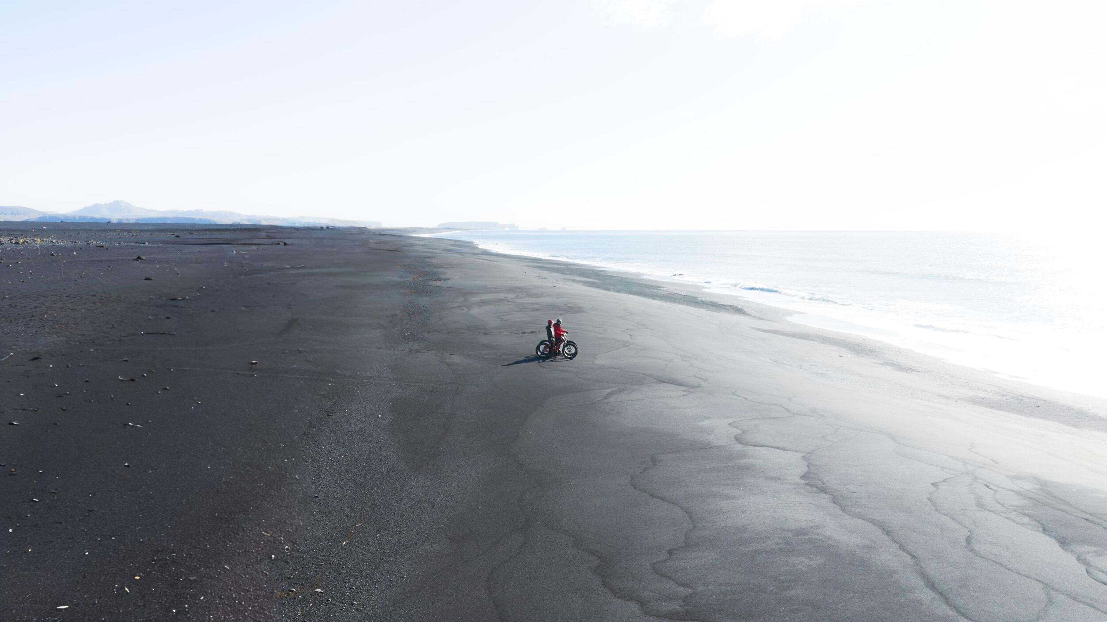 an aerial view of a person riding a bike on a black sandy beach .