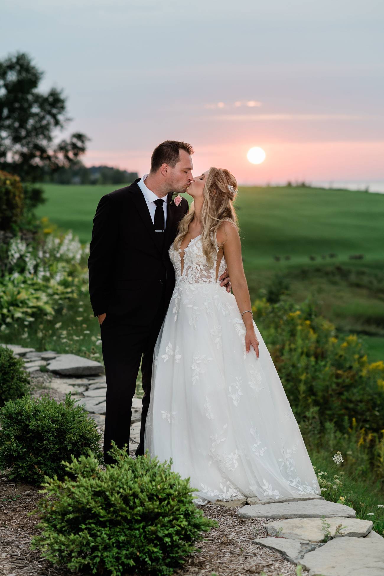 Newlyweds kiss in front of golf course sunset
