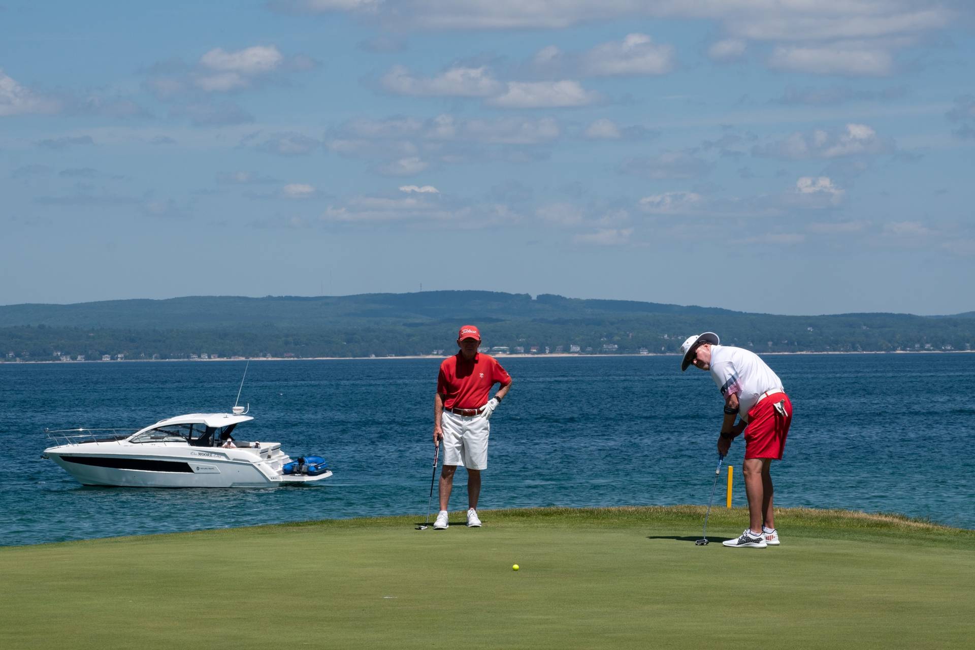 guys golfing with boat in the background