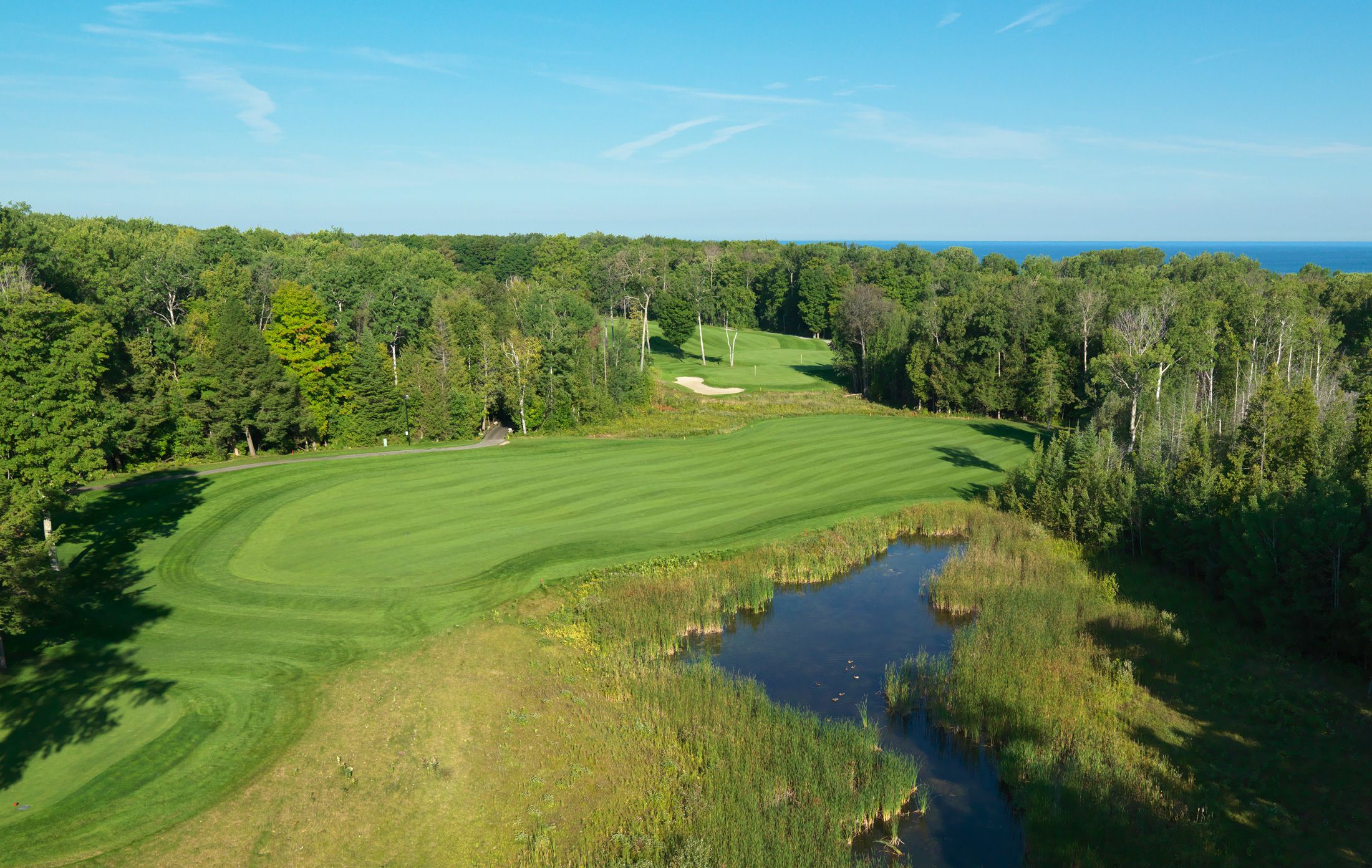 Golf course surrounded by trees, pond, and distant lake, Bay Harbor Golf Club