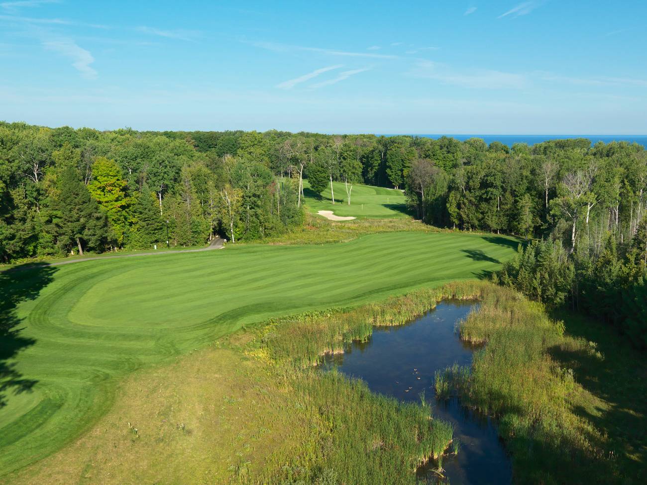 Golf course surrounded by trees, pond, and distant lake, Bay Harbor Golf Club