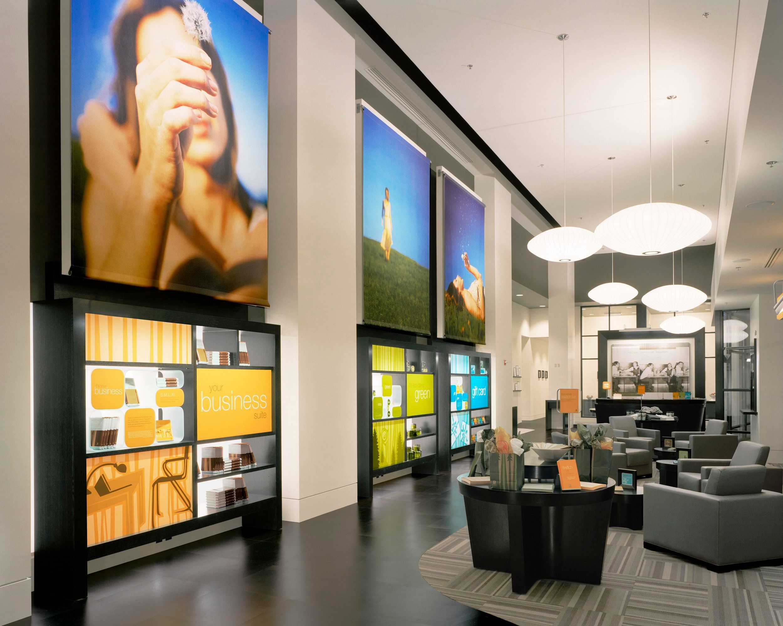 Interior of Umpqua Bank, featuring large banner images of a woman in a field, several lounge chairs, and bright colorful shelves with illustrations and products