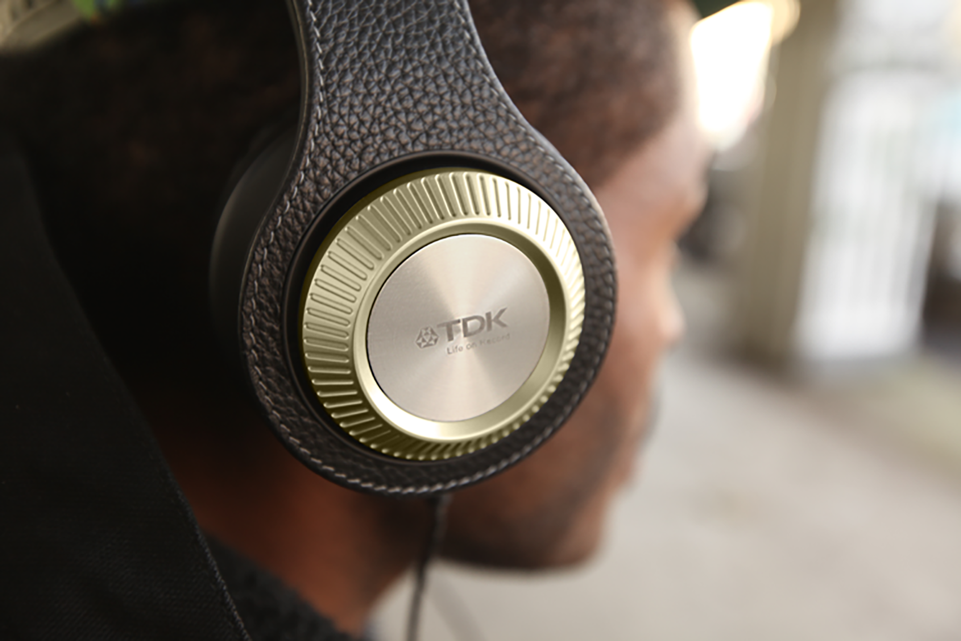 Person wearing black leather over-ear headphones that has a gold ear cover labled “TDK, Life on Record”