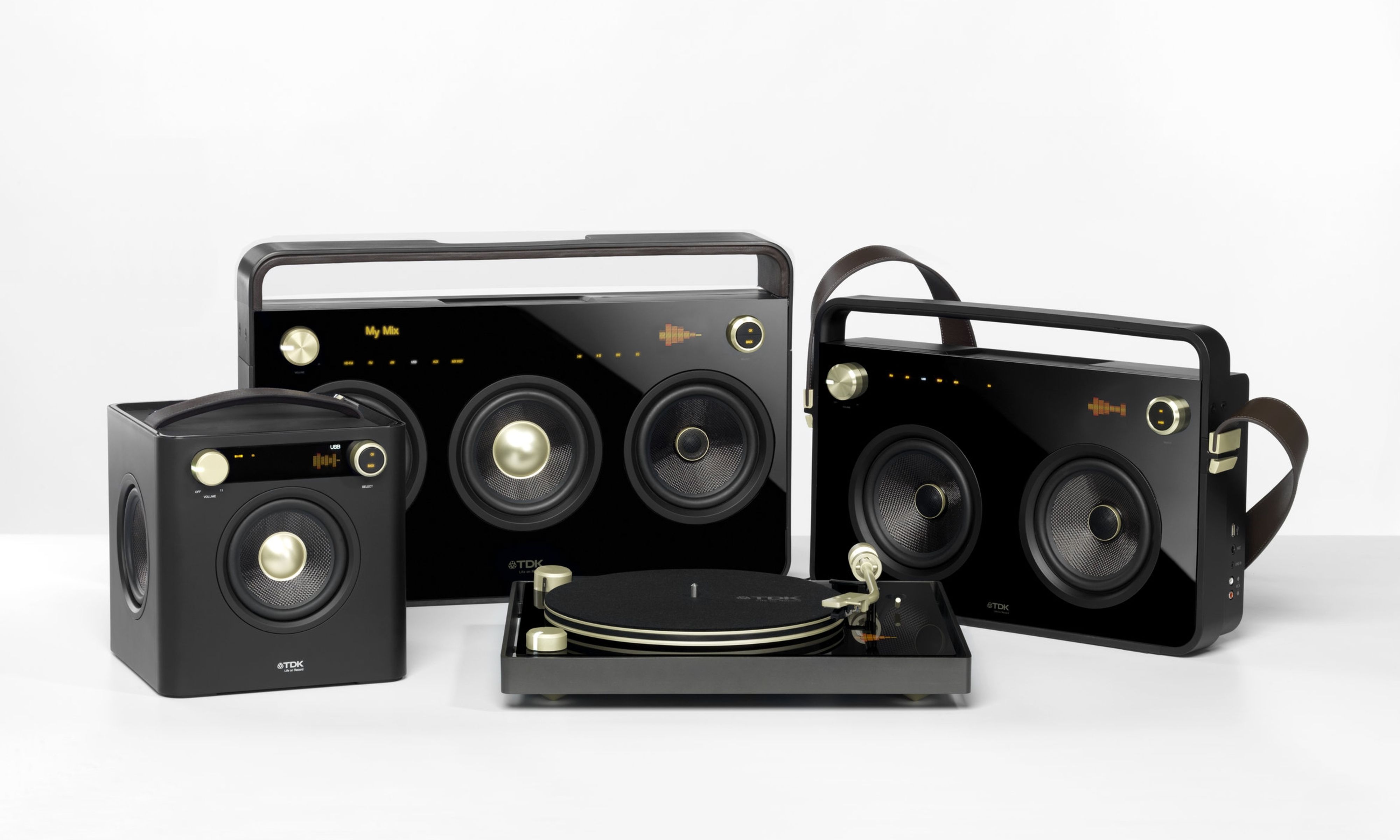 Three black boomboxes and one black record player, all featuring gold hardware and a digital interface with orange coloring