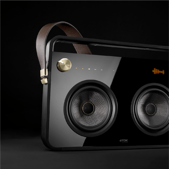 Black boombox with a gold knob in the top left, two speakers in the middle, and a brown leather strap buckled to the side