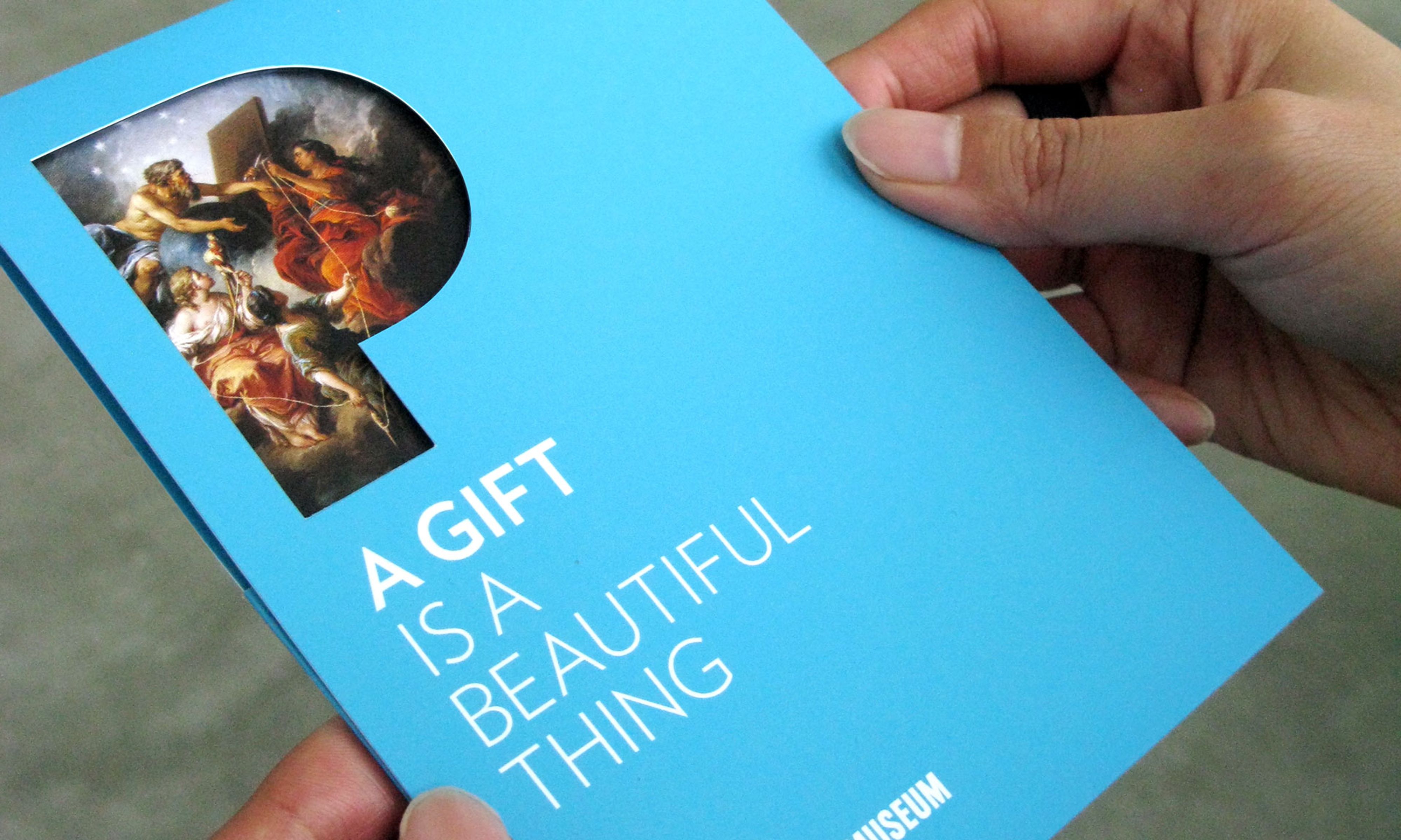 Hands holding a light blue pamphlet that reads “A gift is a beautiful thing”