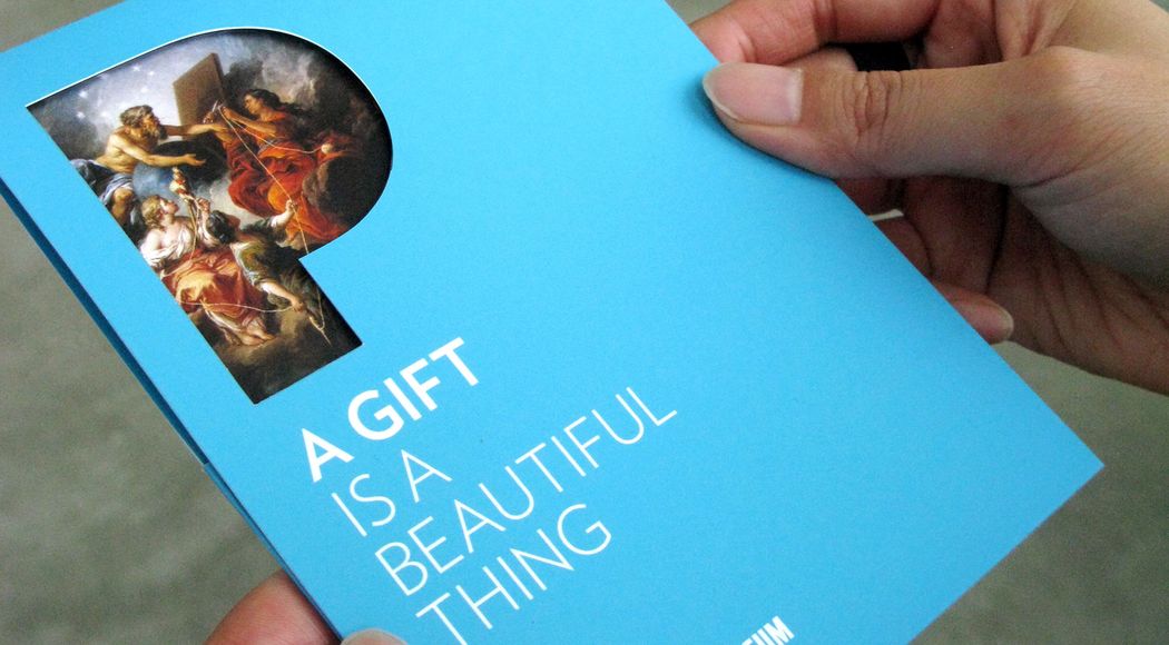 Hands holding a light blue pamphlet that reads “A gift is a beautiful thing”