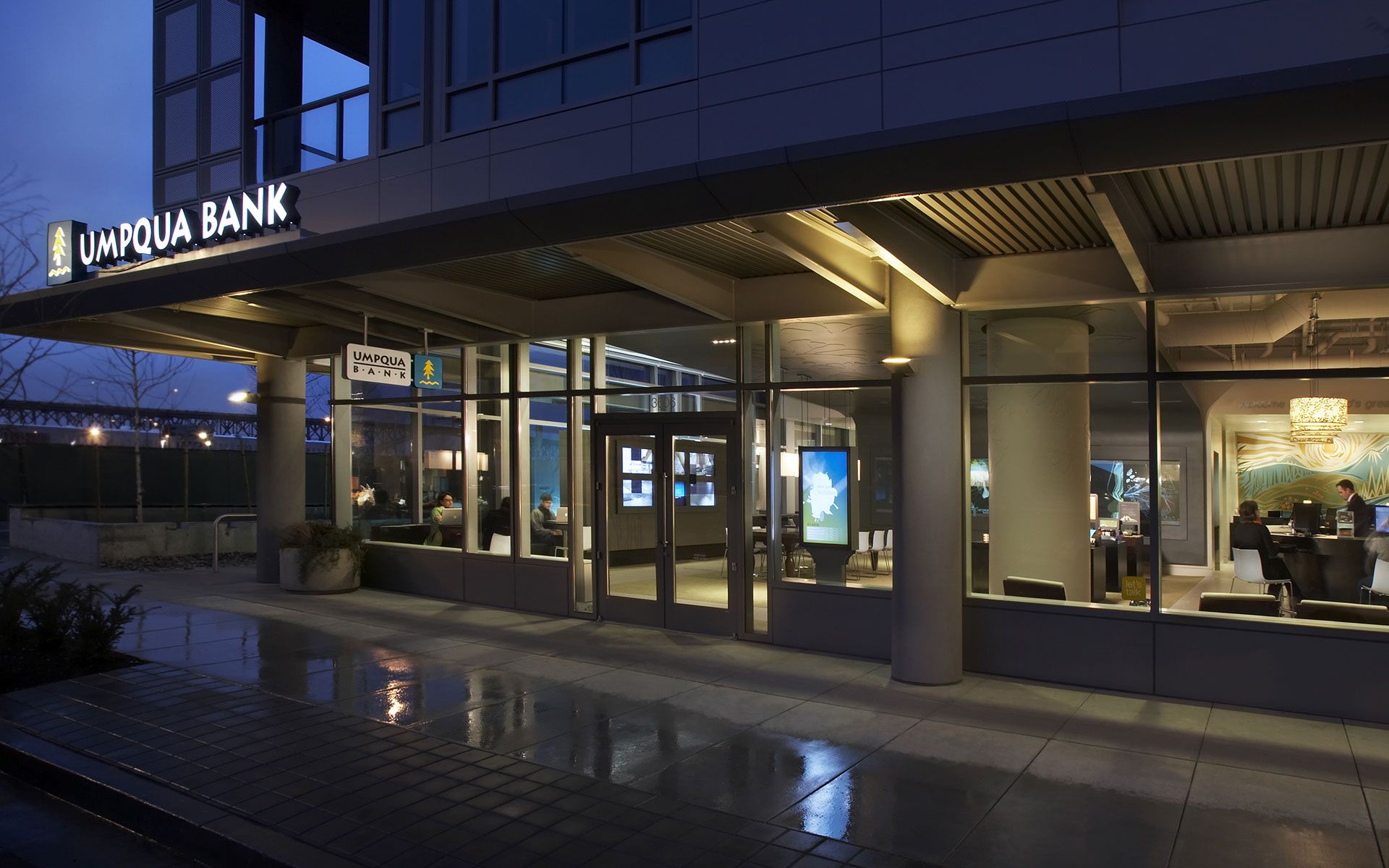 Exterior of Umpqua Bank, featuring large glass windows and doors, with customers 