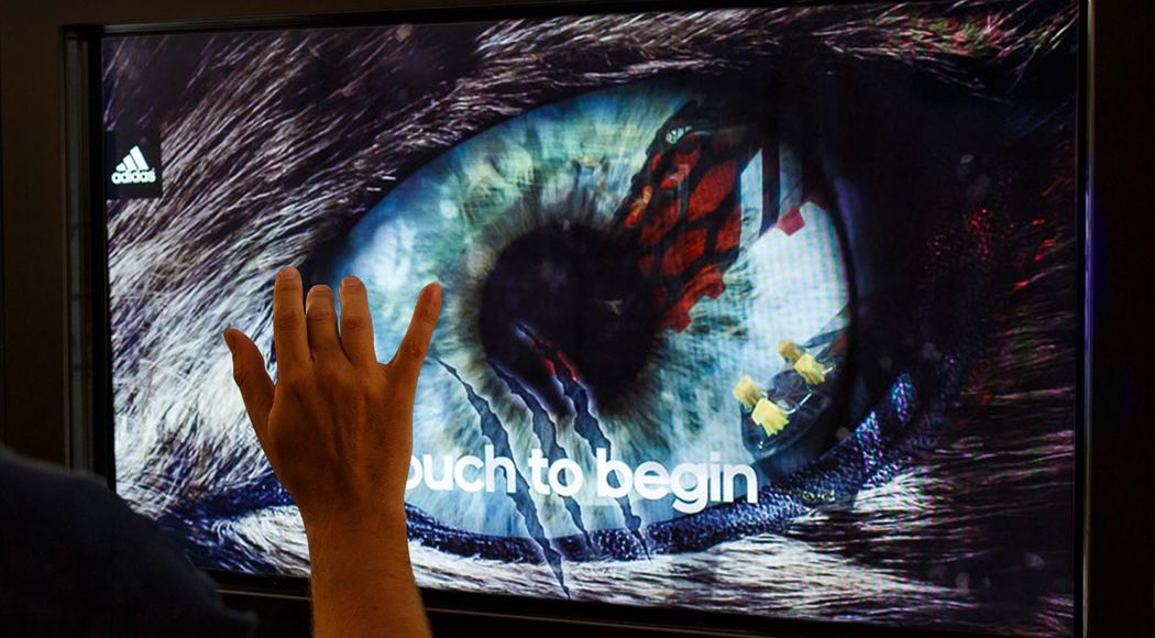 Hand touching a touch screen showing a close up of a wolf’s eye that reads “Touch to begin”
